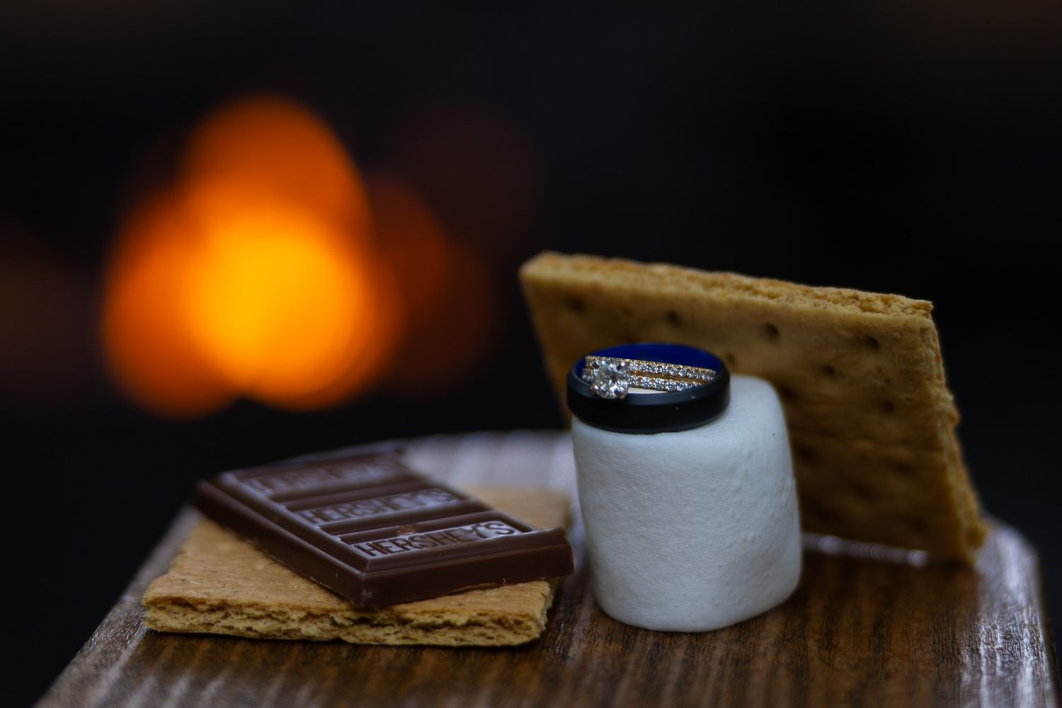 S'mores ingredients including graham crackers, chocolate bar, and marshmallow arranged near a glowing campfire.