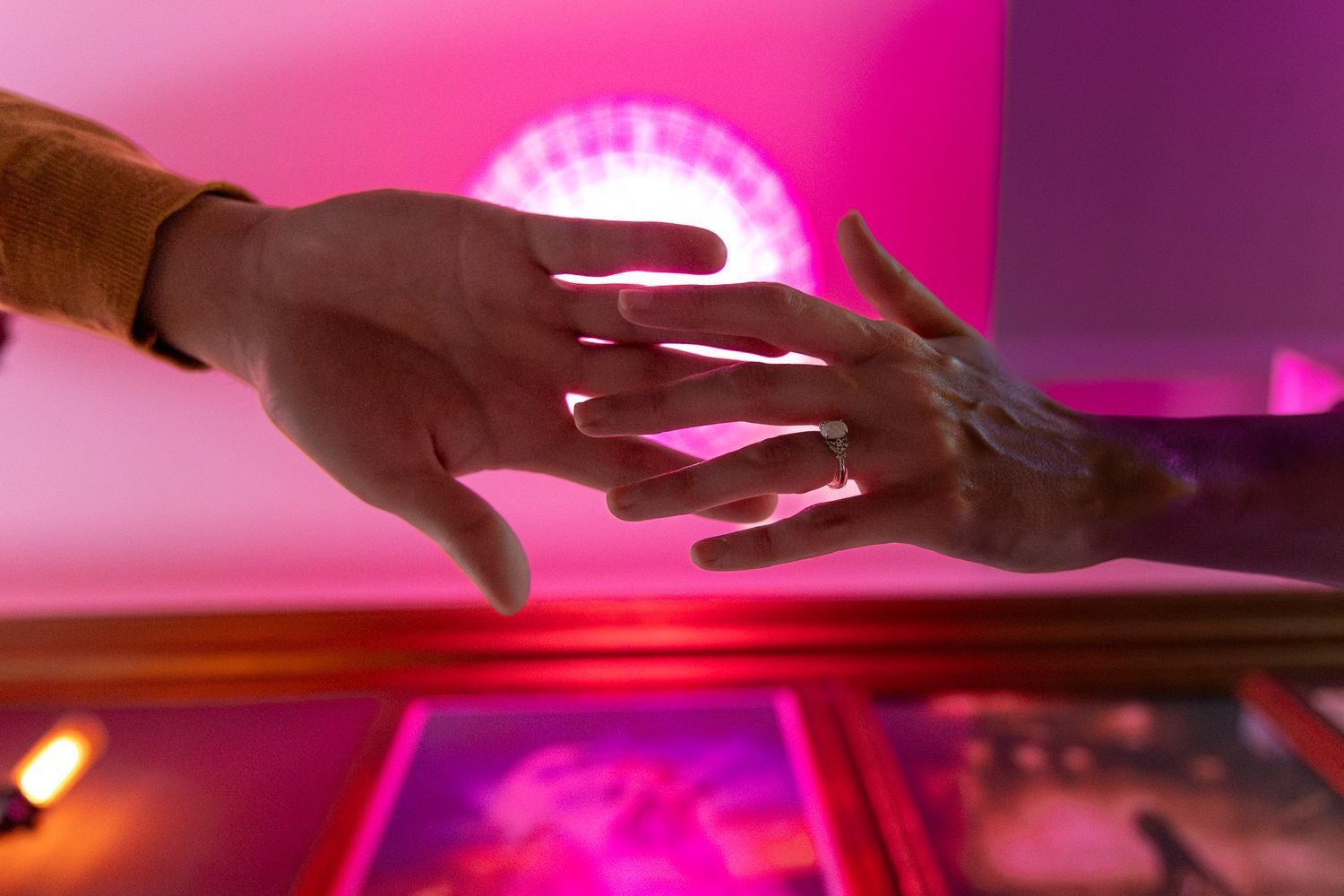 Two hands reaching toward each other under pink neon lights in romantic gesture.