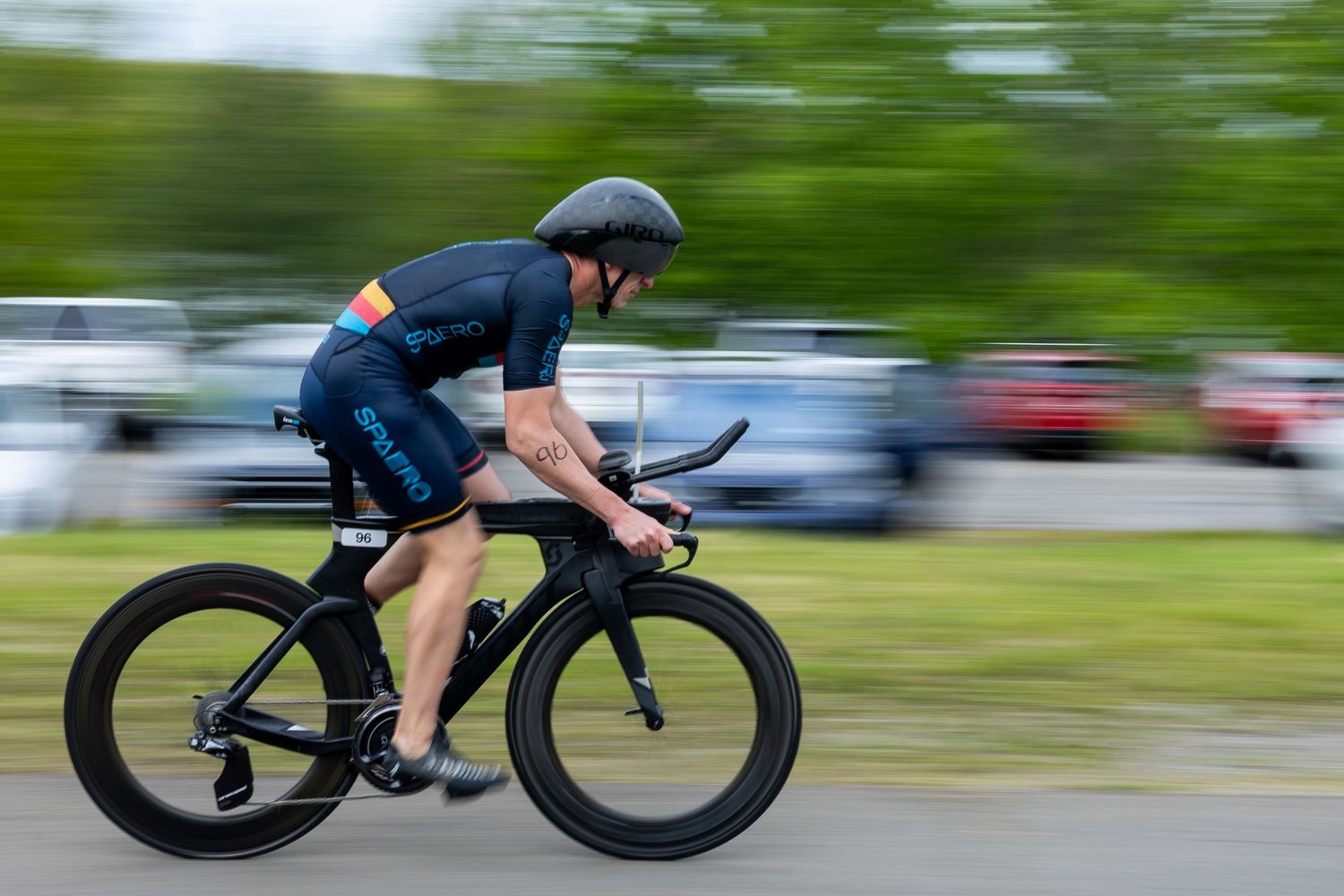 Cyclist in aerodynamic position racing on a black time trial bike wearing a blue jersey and helmet.
