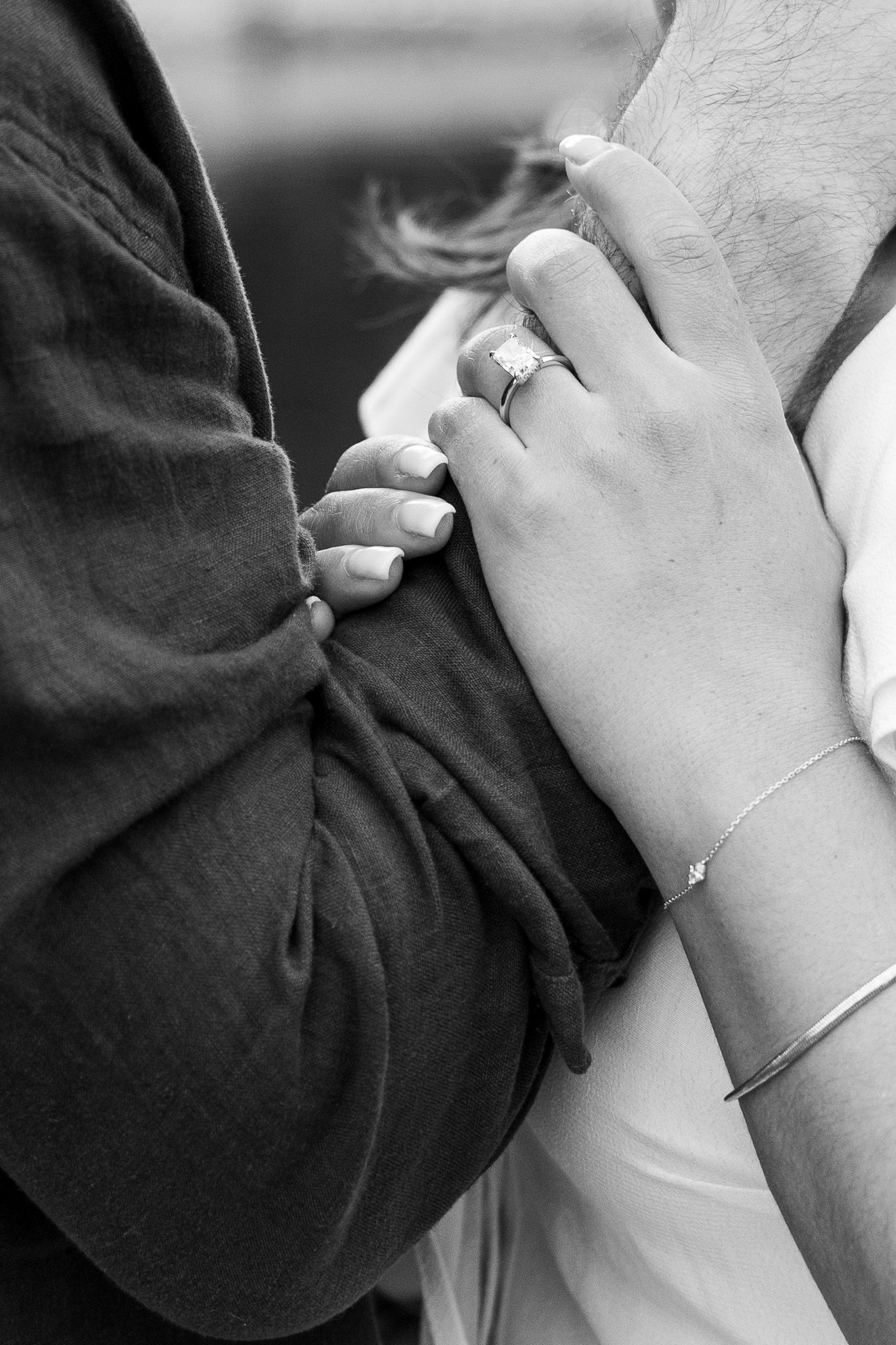 Black and white close-up of couple's hands showing diamond engagement ring and gold bracelet.