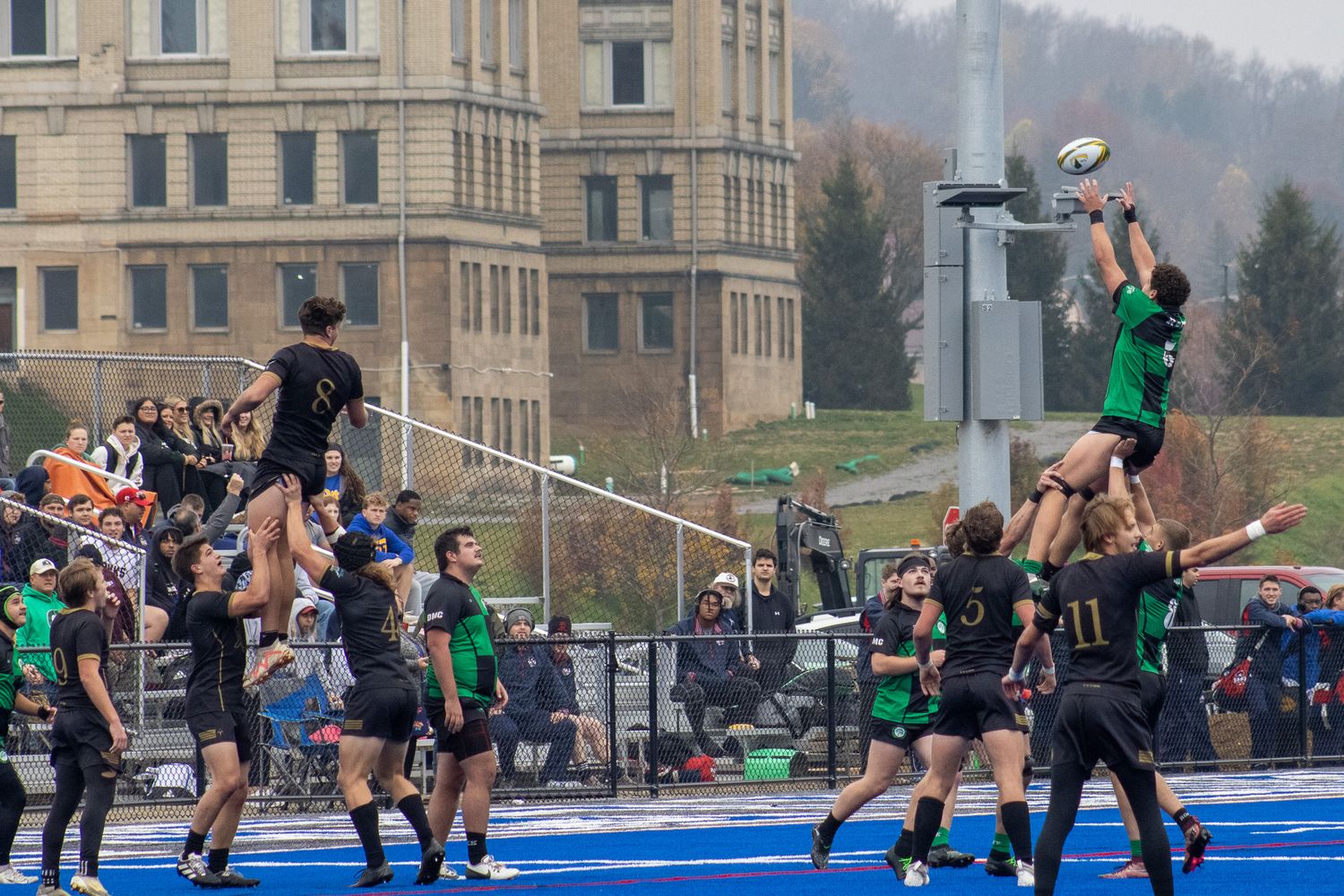 Rugby players compete in a lineout during a match between green and black uniformed teams.