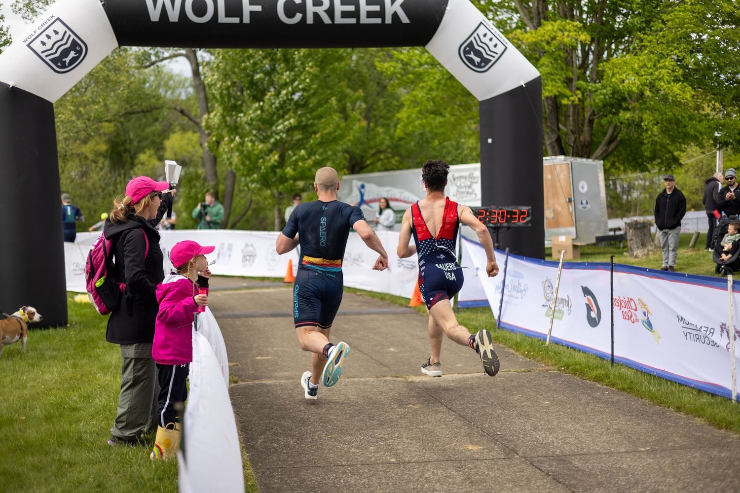 Two triathletes cross the finish line at Wolf Creek race event as spectators cheer them on.