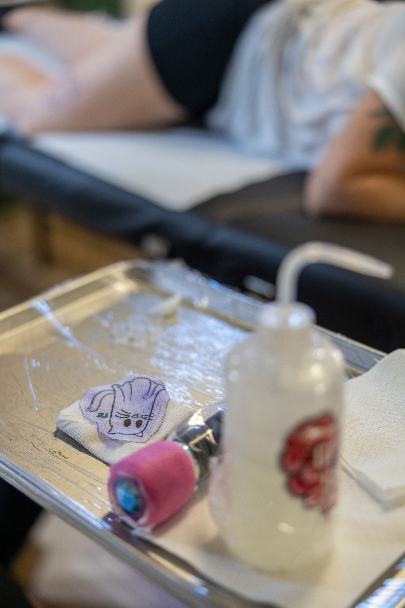 Tattoo studio tray with pink ink cap, stencil paper, and a spray bottle ready for a tattooing session.