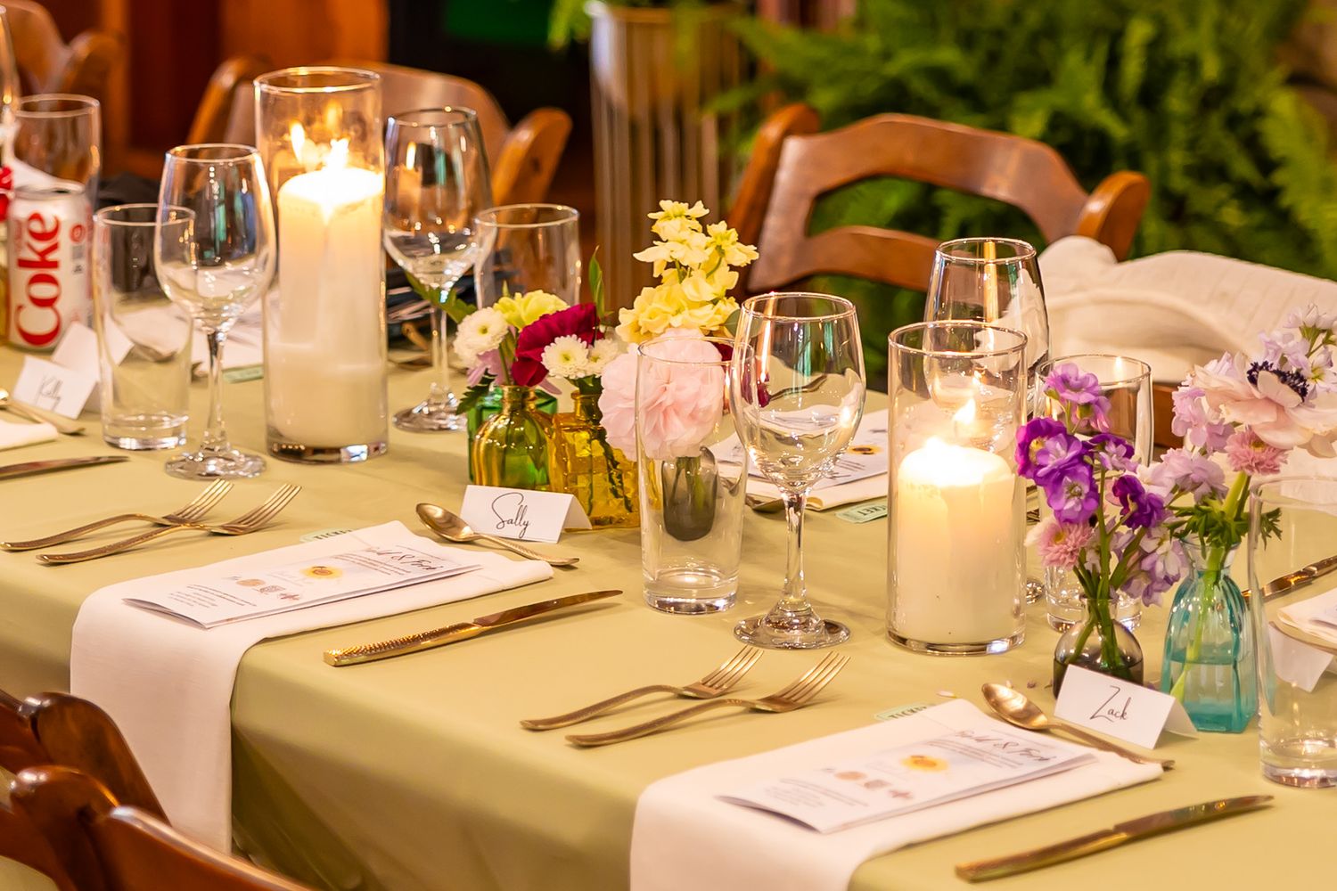 An elegantly set dining table with candles, floral arrangements, wine glasses, and place cards for a special event.