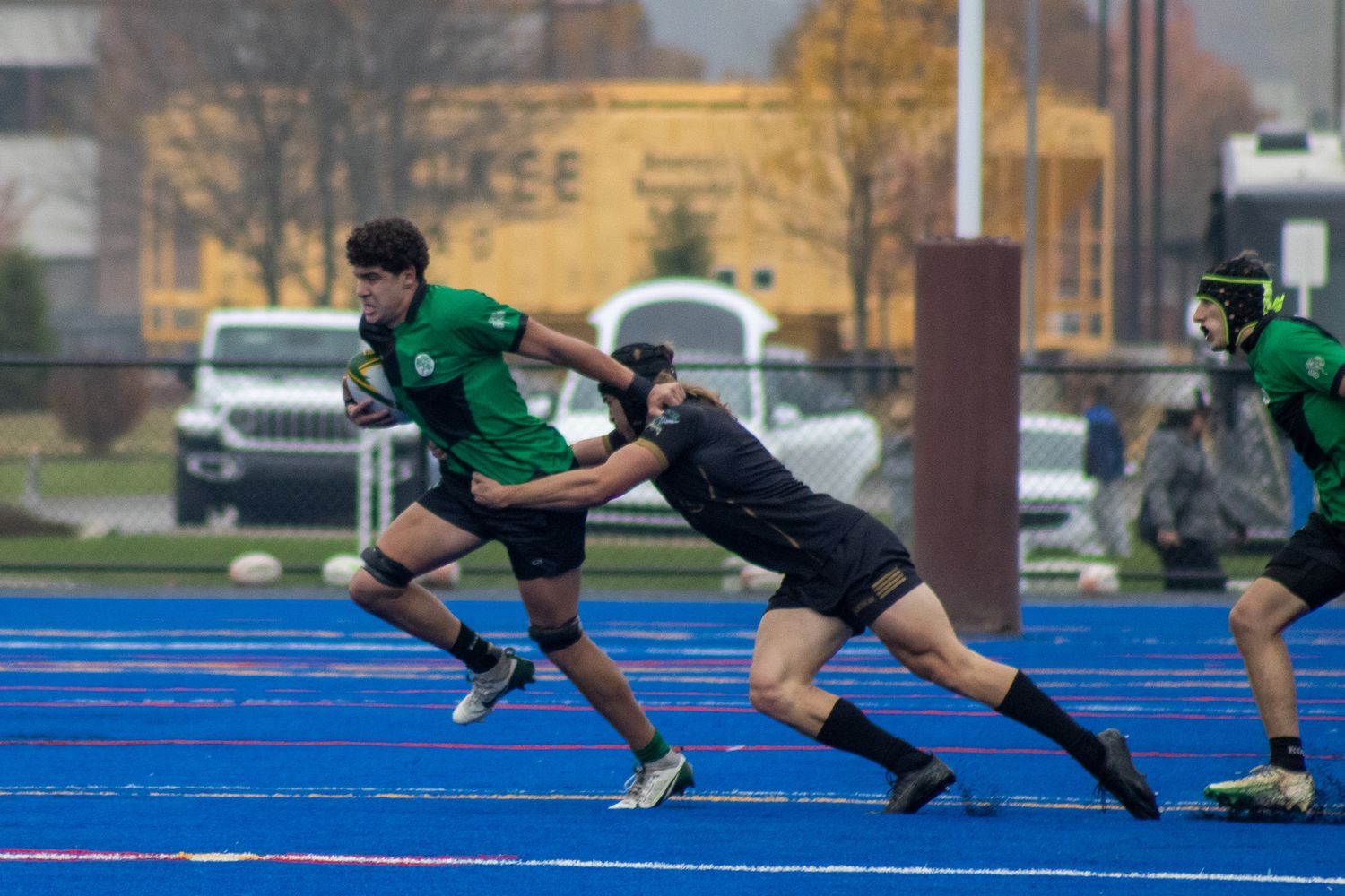 Green-uniformed rugby player breaks away from a tackle during a youth rugby match on a blue field.
