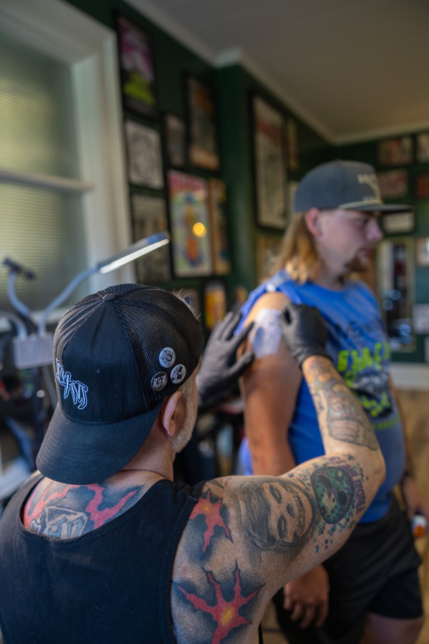 Heavily tattooed artist tattooing a client's arm in a decorated tattoo studio.