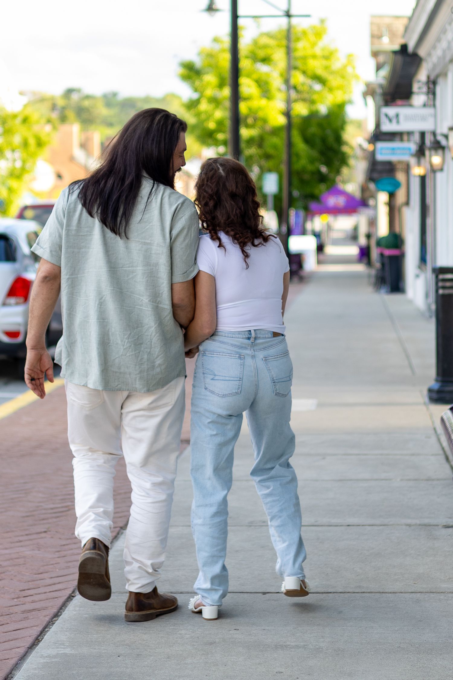 Couple walking hand in hand down a sunny small town sidewalk.