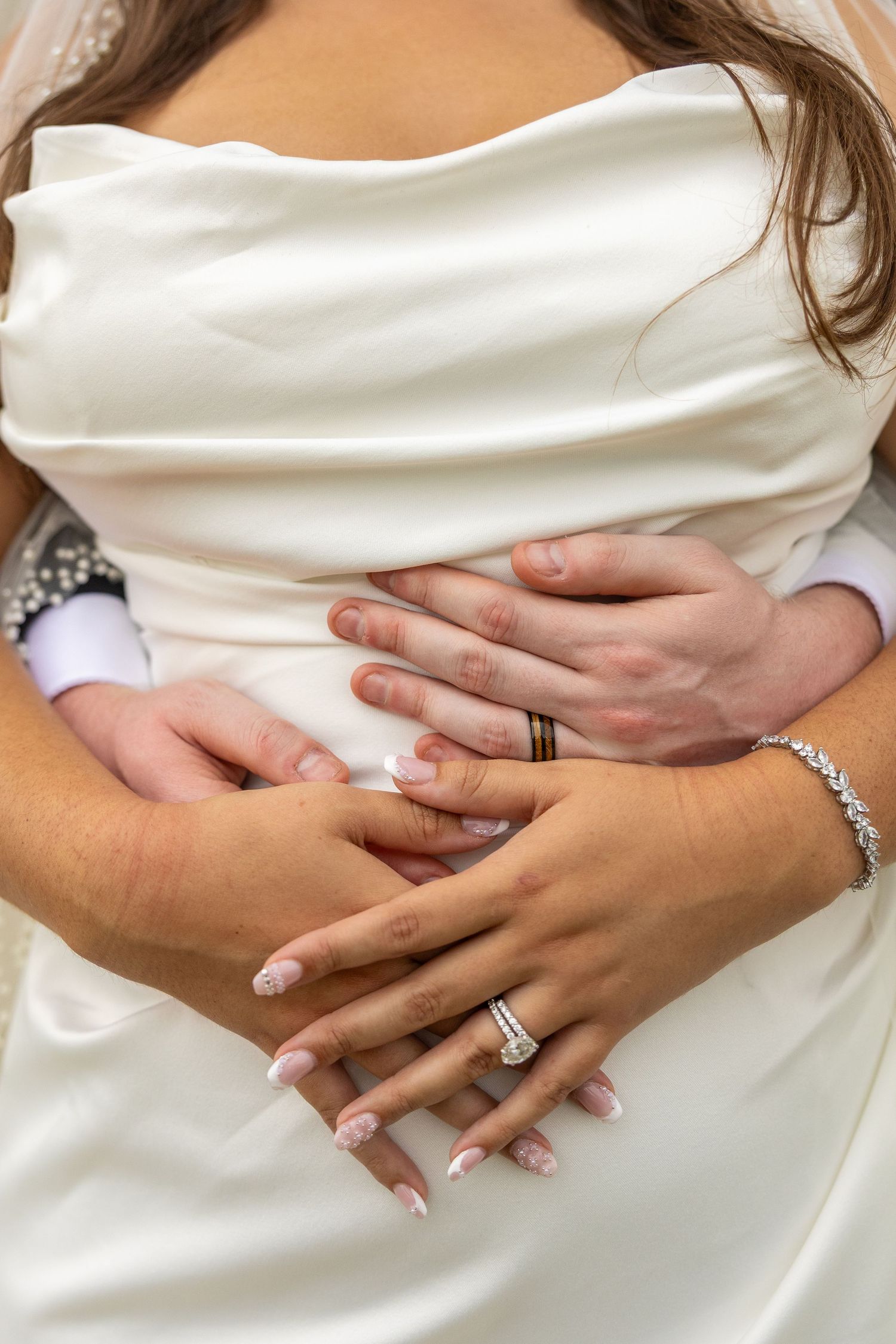 Bride and groom hands clasped together showing diamond engagement ring and wedding band during wedding ceremony.