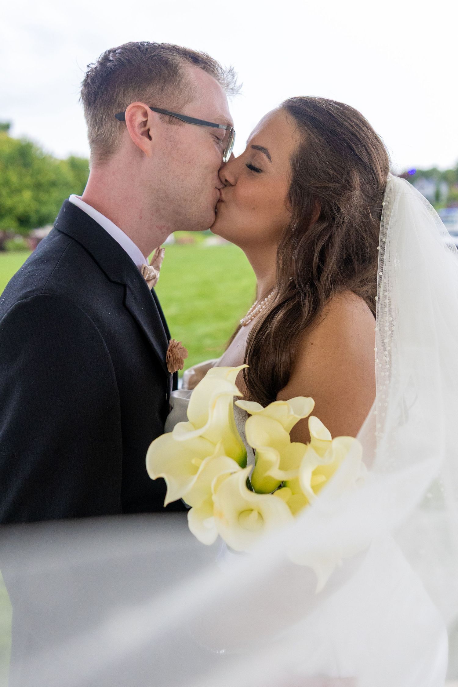 Bride and groom sharing a romantic kiss on their wedding day, bride holding white calla lily bouquet.