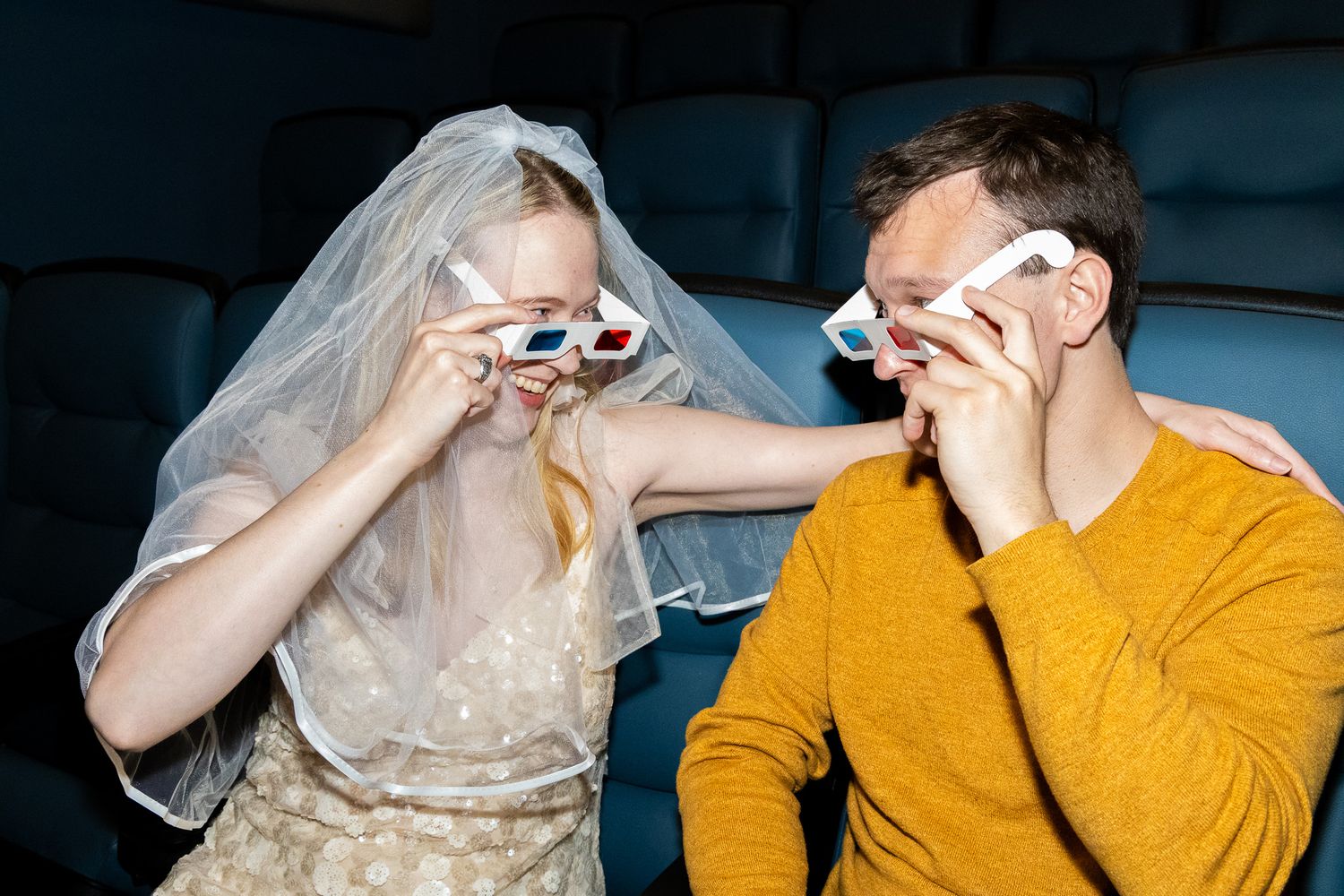 Bride and groom putting on 3D glasses together at a movie theater.