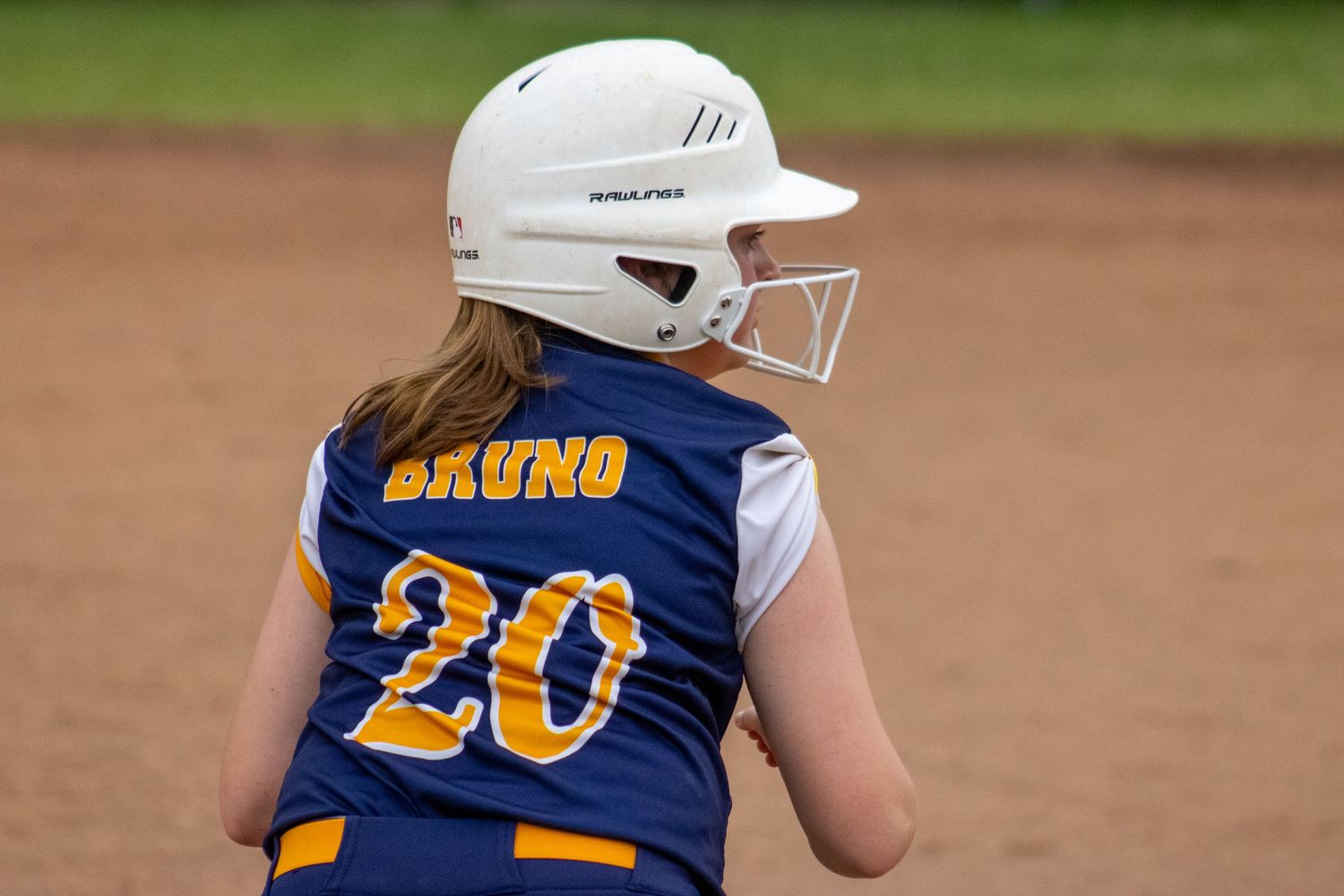 Youth softball player wearing Bruno number 20 jersey and batting helmet stands on field.