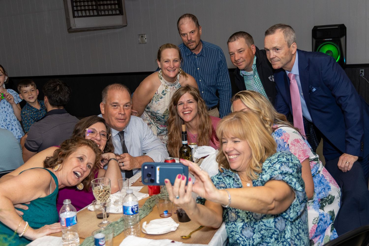 Group of adults smiling and taking a selfie together at a casual indoor party or banquet event.