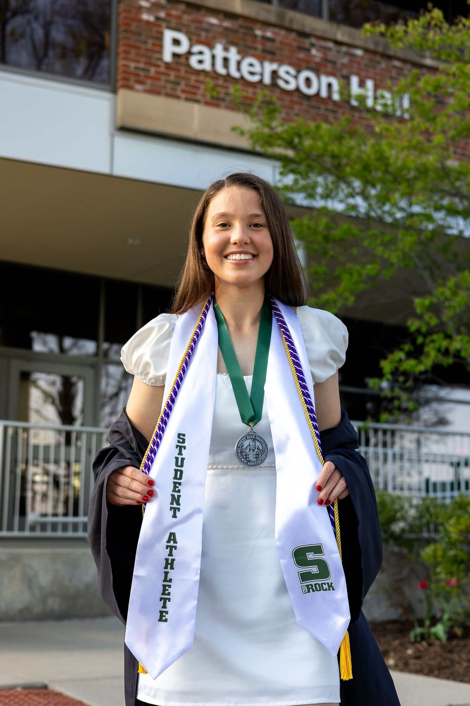 Smiling graduate displays Student Athlete stole and medal outside Patterson Hall at Slippery Rock University.