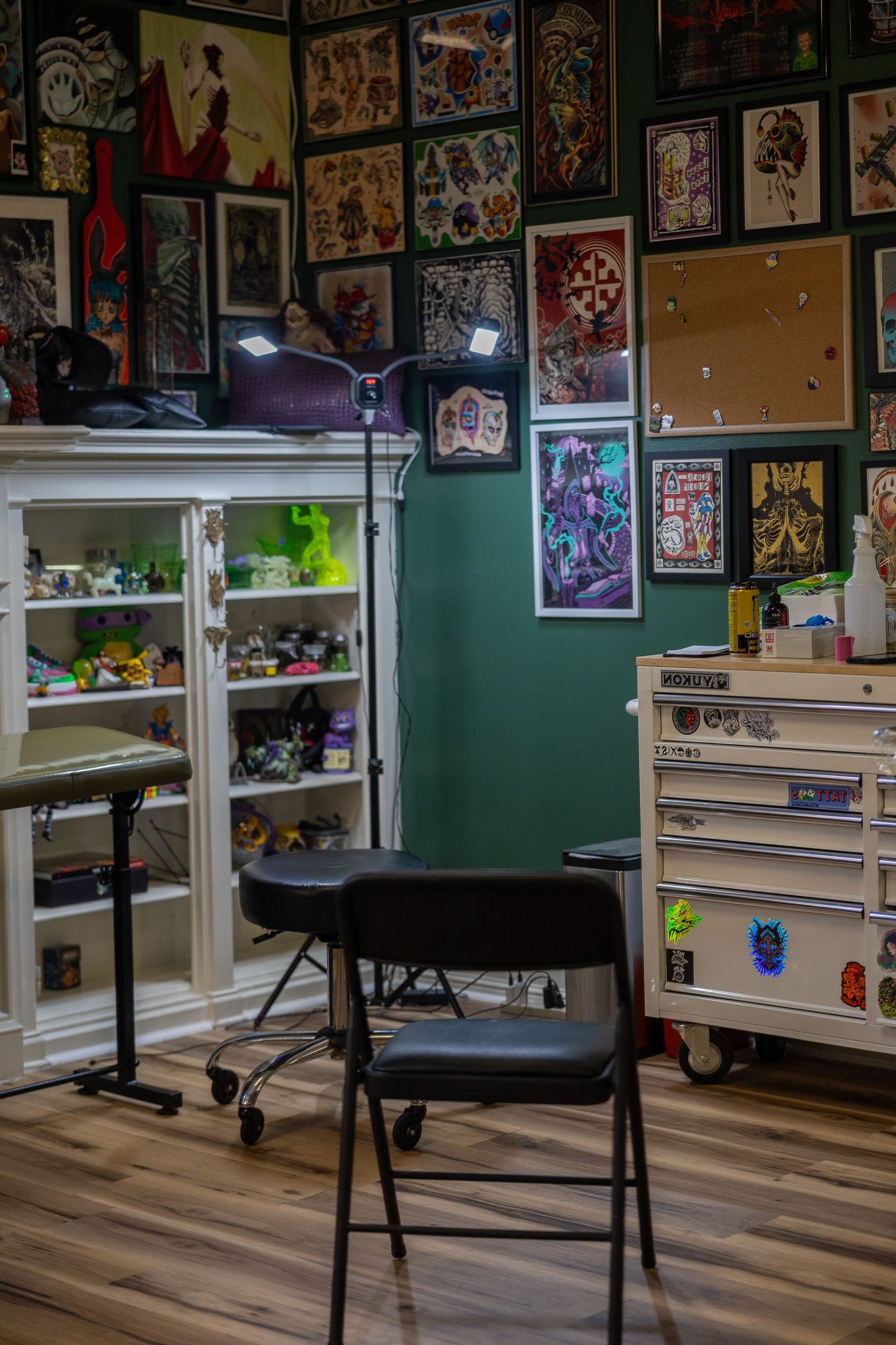 Interior of a tattoo studio with art-covered green walls, a black chair, shelving, and a tool cabinet.