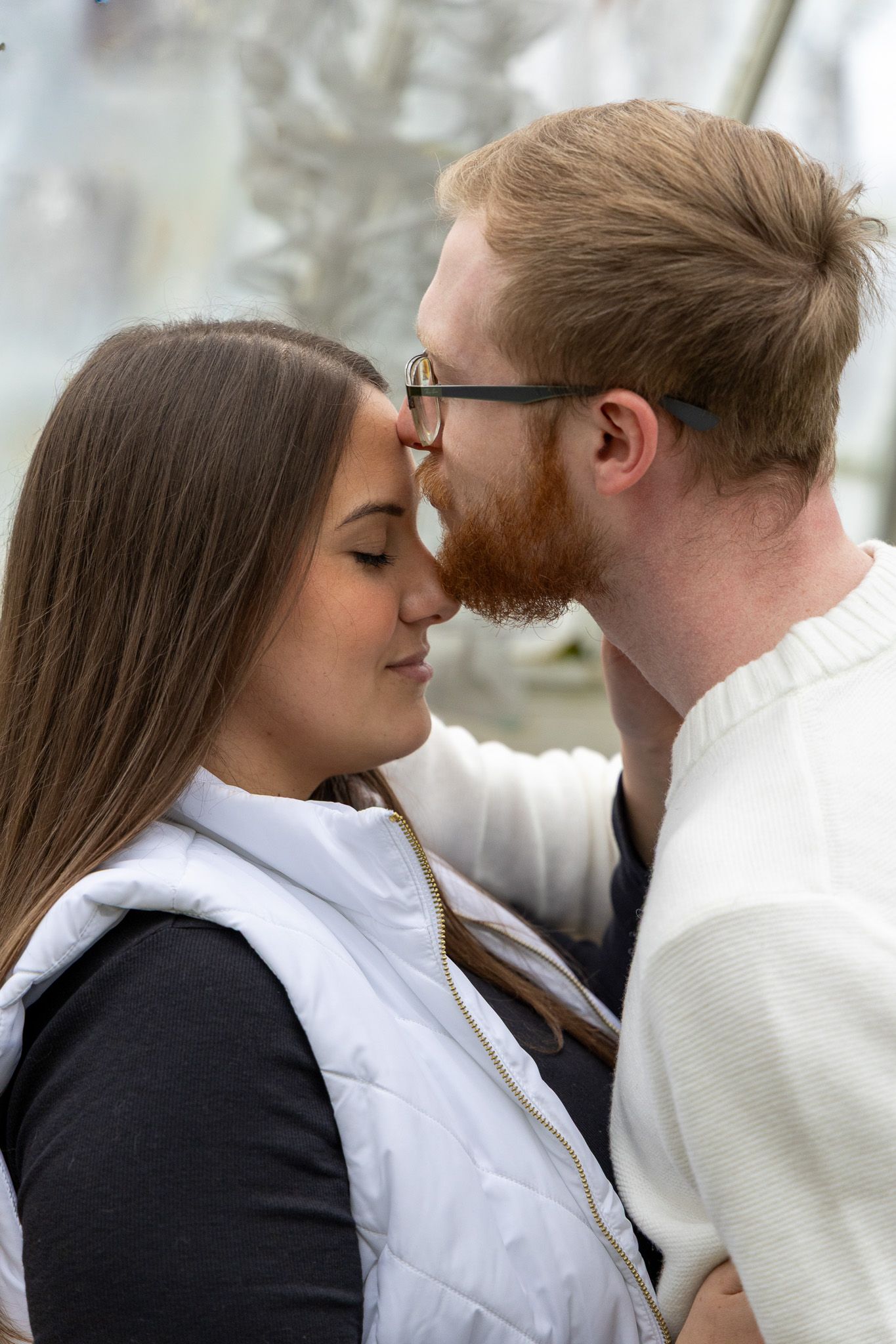 A couple sharing a tender kiss, the man with a red beard and glasses holding the womans face gently.