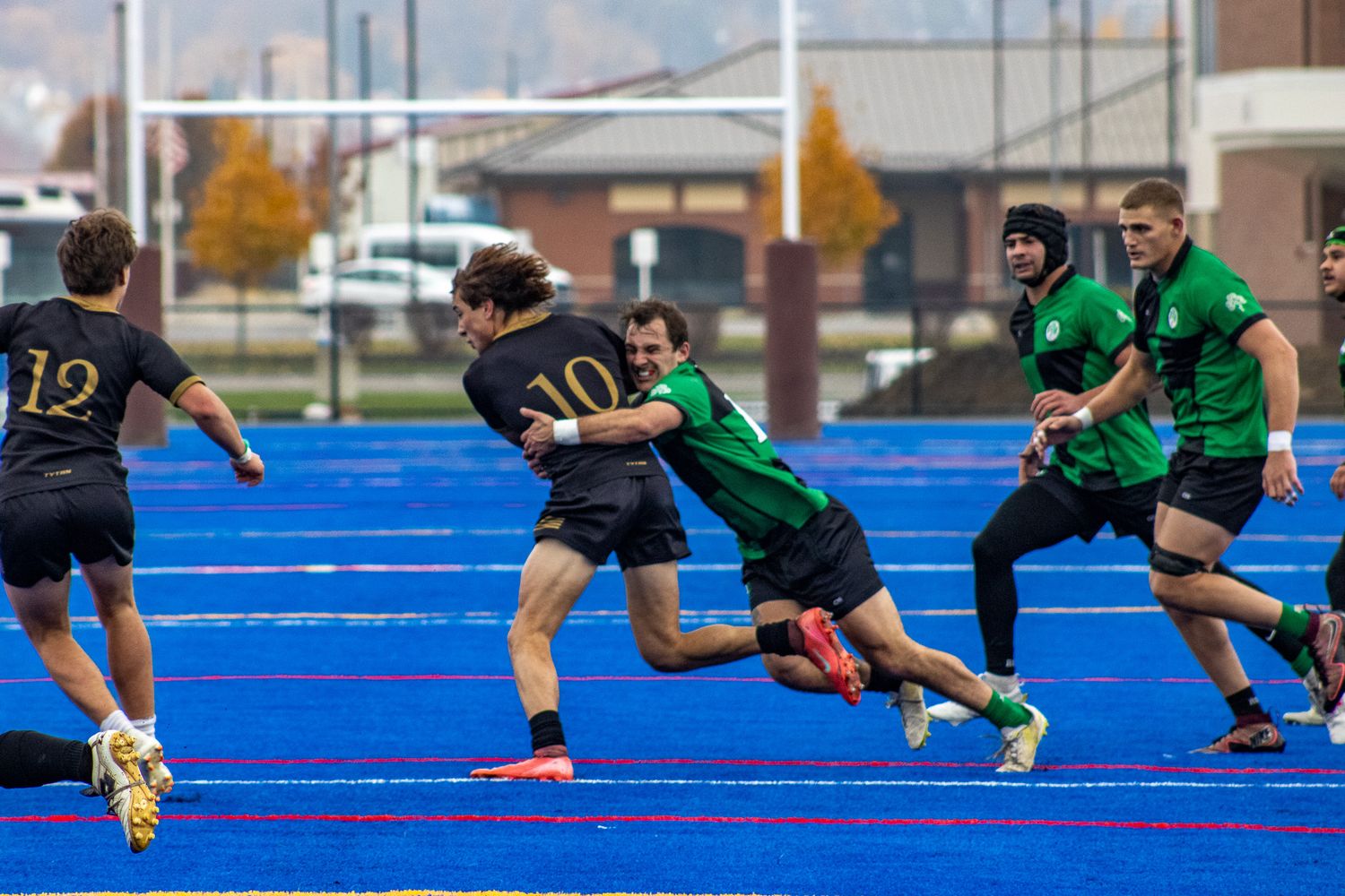 Green-uniformed rugby player tackles a black #10 jersey opponent during a youth rugby match.