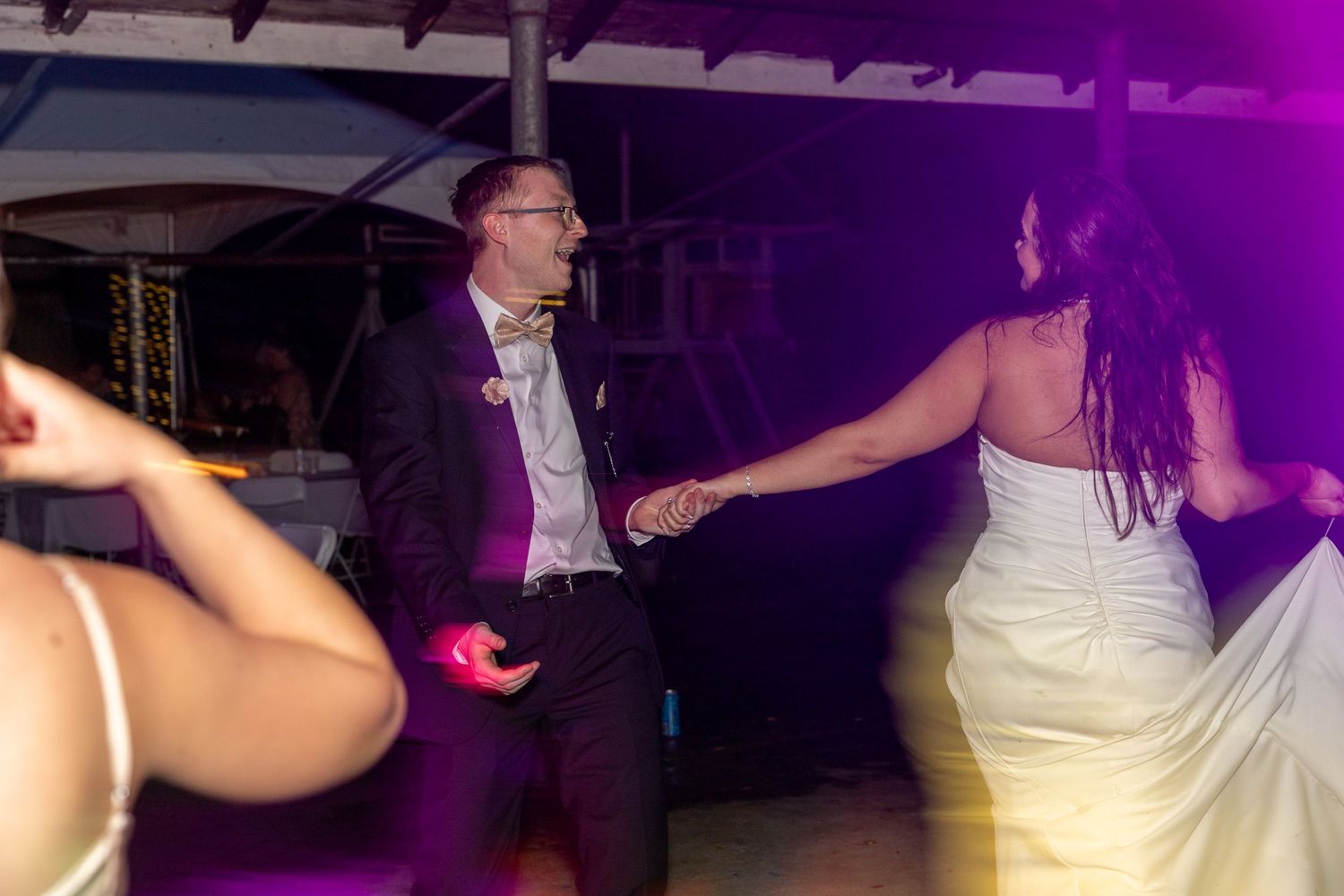 Bride and groom dancing joyfully at their wedding reception under purple lights.