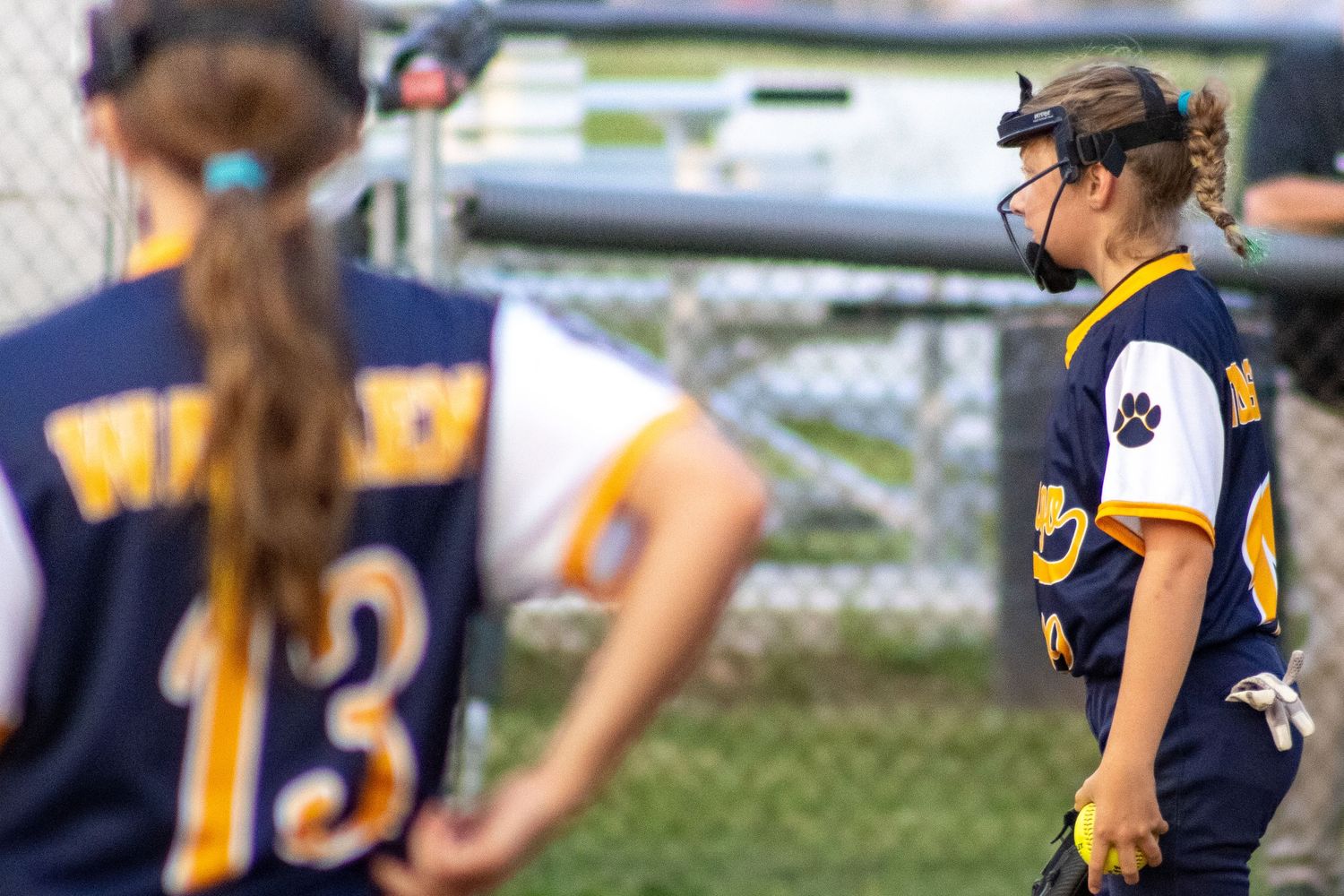 Two youth softball players in navy Wildcats uniforms stand on field during game.