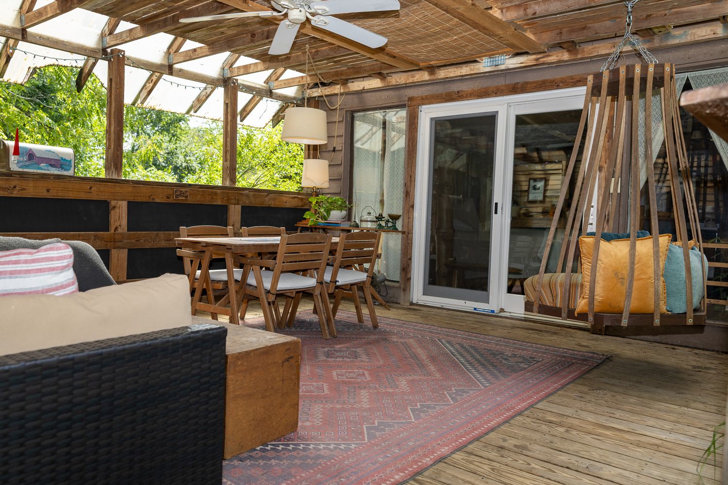 Covered wooden deck with dining set, wicker sofa, patterned rug, ceiling fan, and French doors leading indoors.
