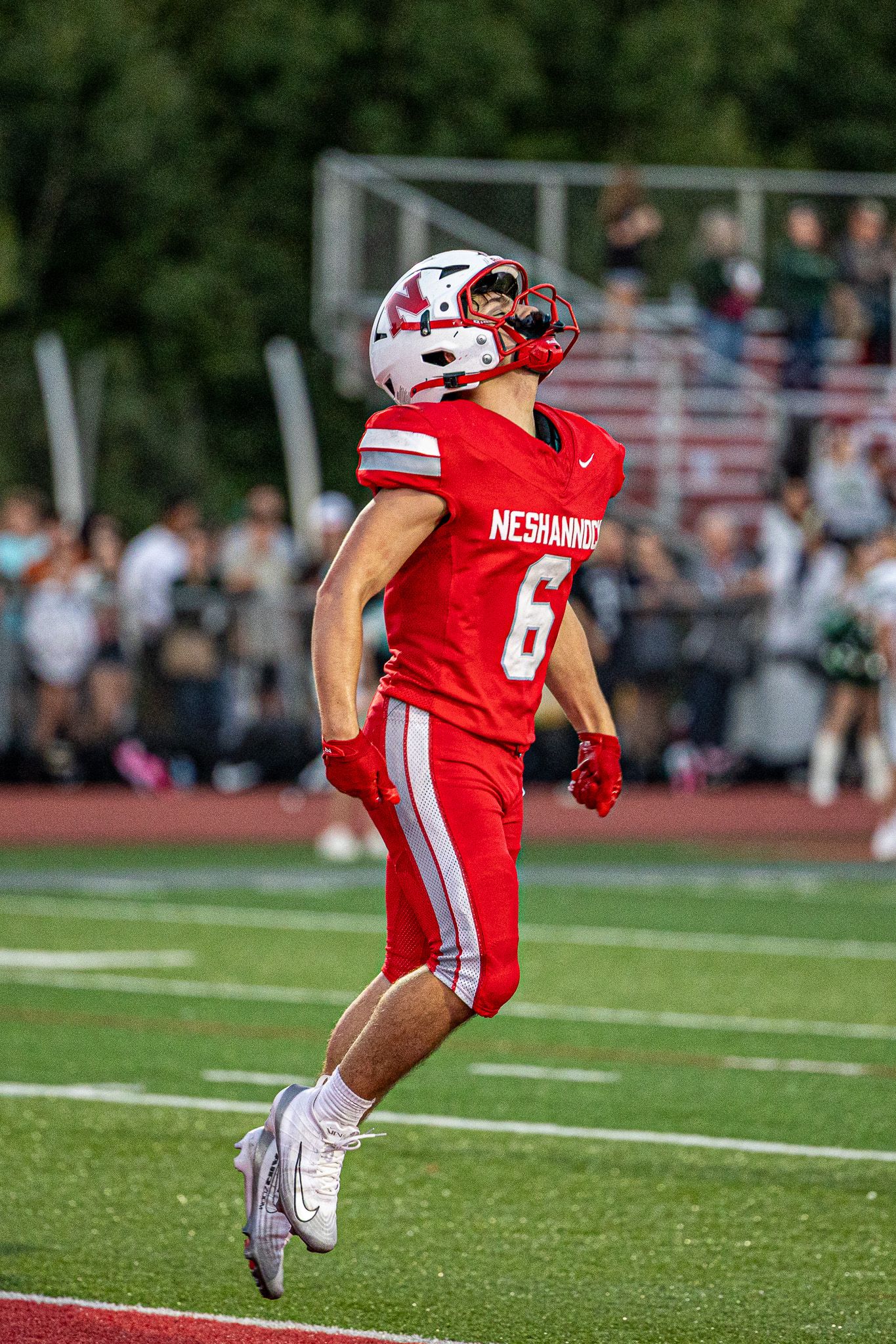 Neshannock football player #6 in red uniform runs on track during a high school game with crowd in background.