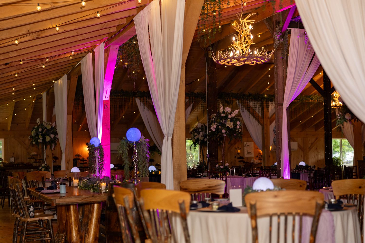 Elegant barn wedding reception venue decorated with pink uplighting, draped fabric, and floral centerpieces.