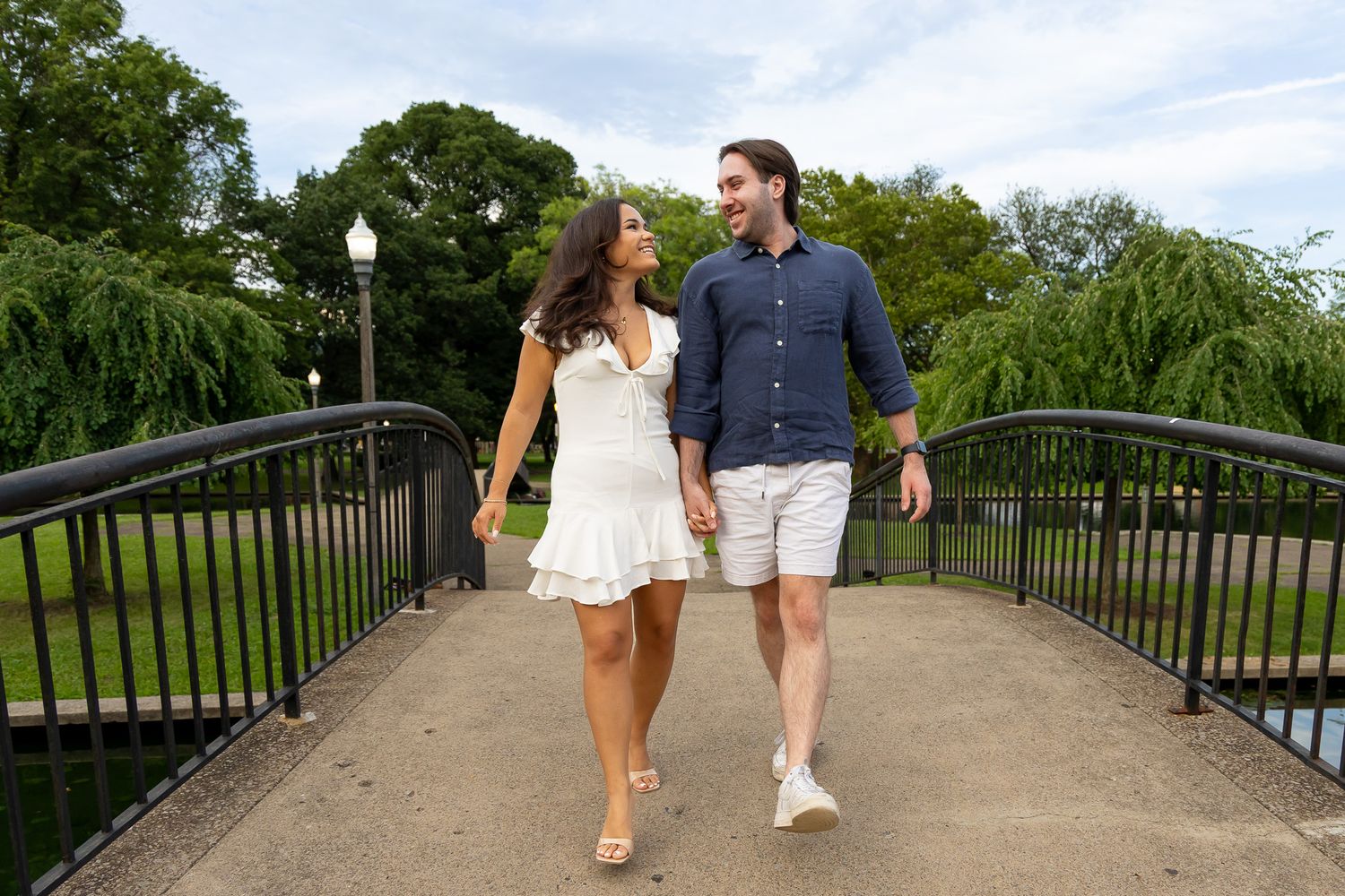 Smiling couple holding hands and laughing while walking across a bridge during outdoor engagement photos.