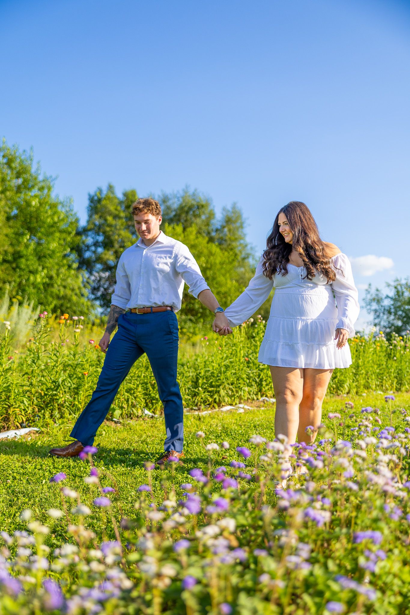 Happy couple holding hands walking through a vibrant wildflower meadow on a sunny day.