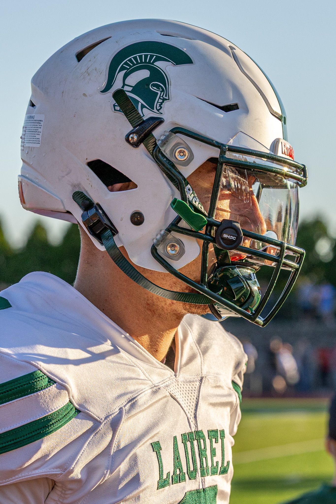 Laurel Spartans football player wearing white helmet with Spartan logo and green face mask on sunny game day.
