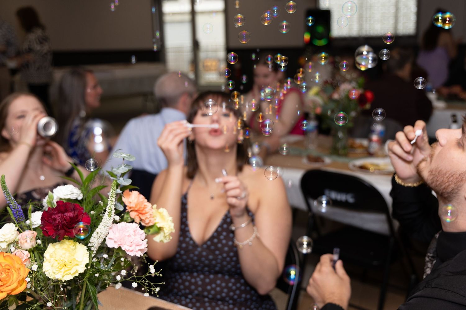 Guests blowing colorful soap bubbles at a wedding reception with floral centerpieces on the table.