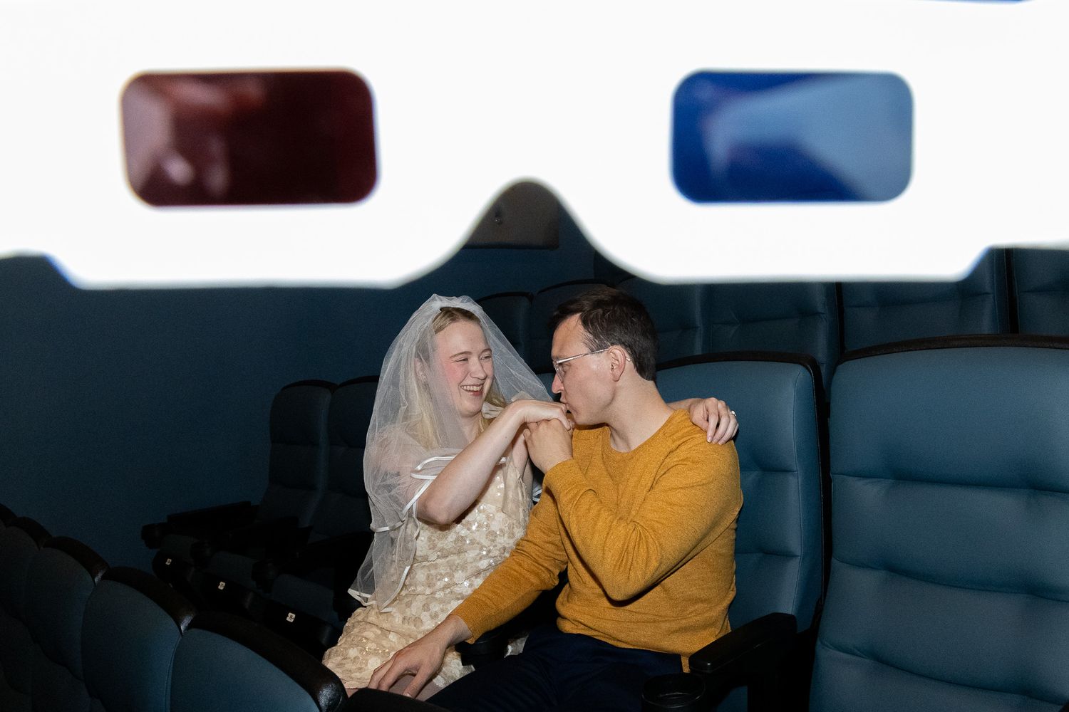 Couple sharing a romantic moment at the cinema, man kissing woman's hand affectionately.