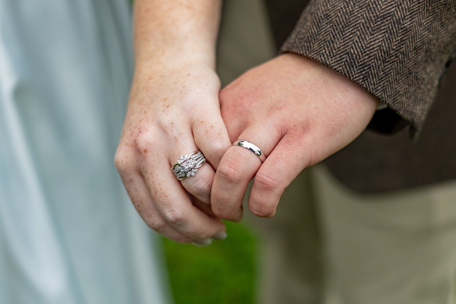 Close-up of newlywed couple holding hands showing wedding and engagement rings outdoors.