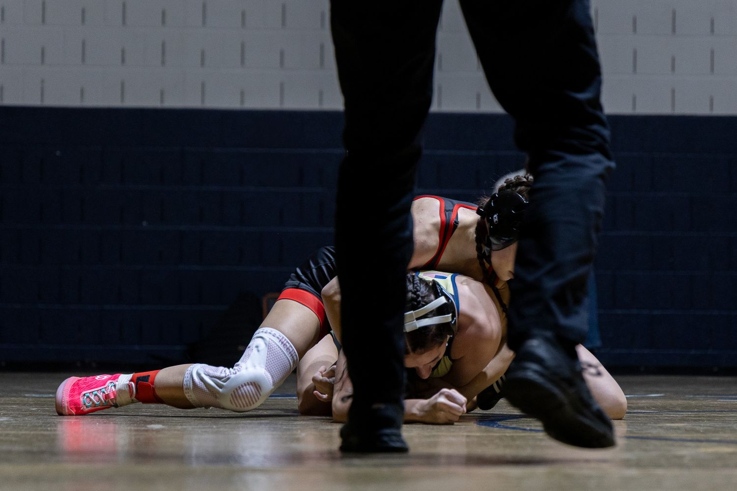 Female wrestler pins opponent to the mat during an indoor wrestling competition.
