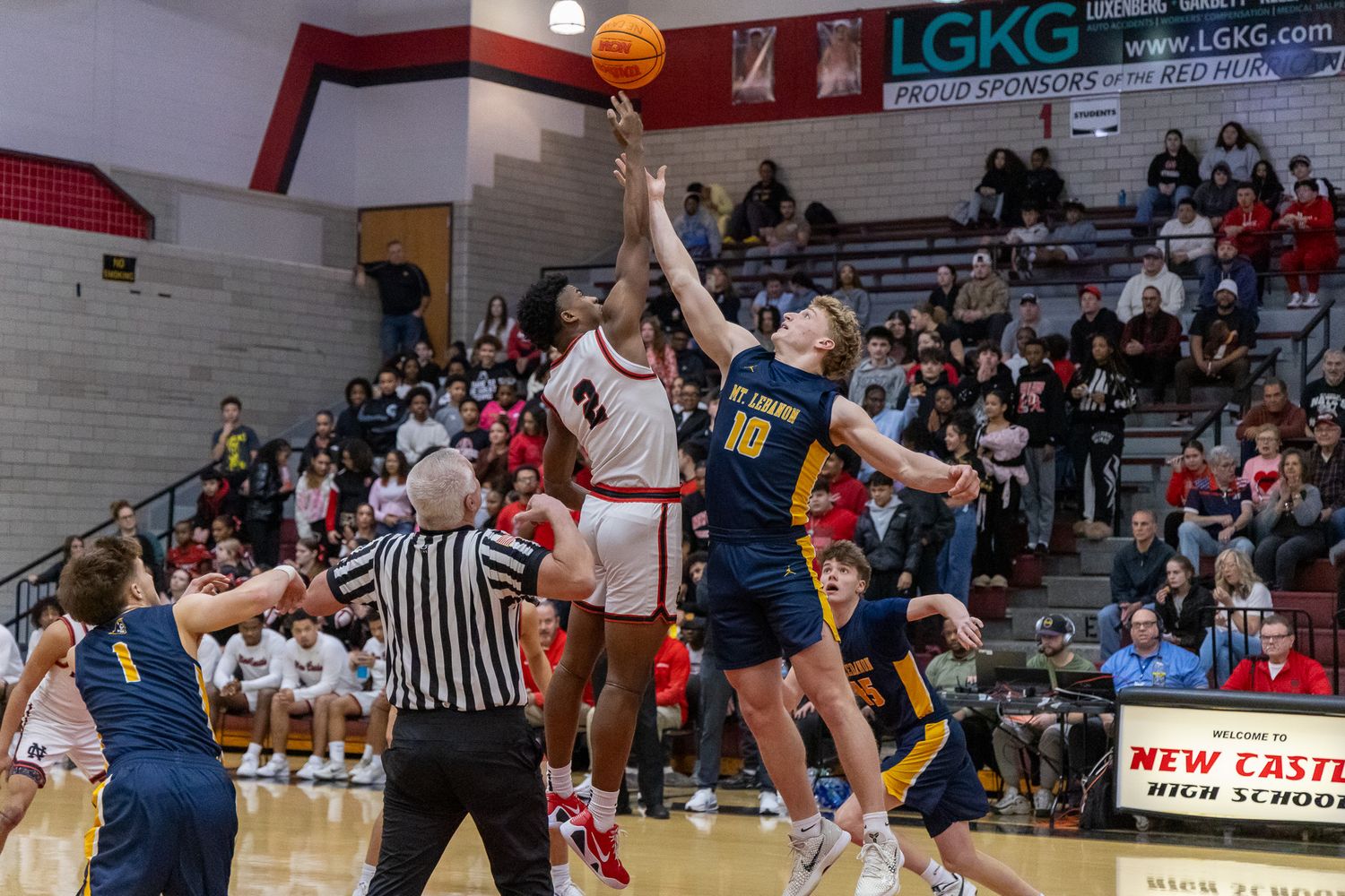 Jump ball tip-off between Ne-Ca-Hi and Mt. Lebanon players at a packed high school basketball game.