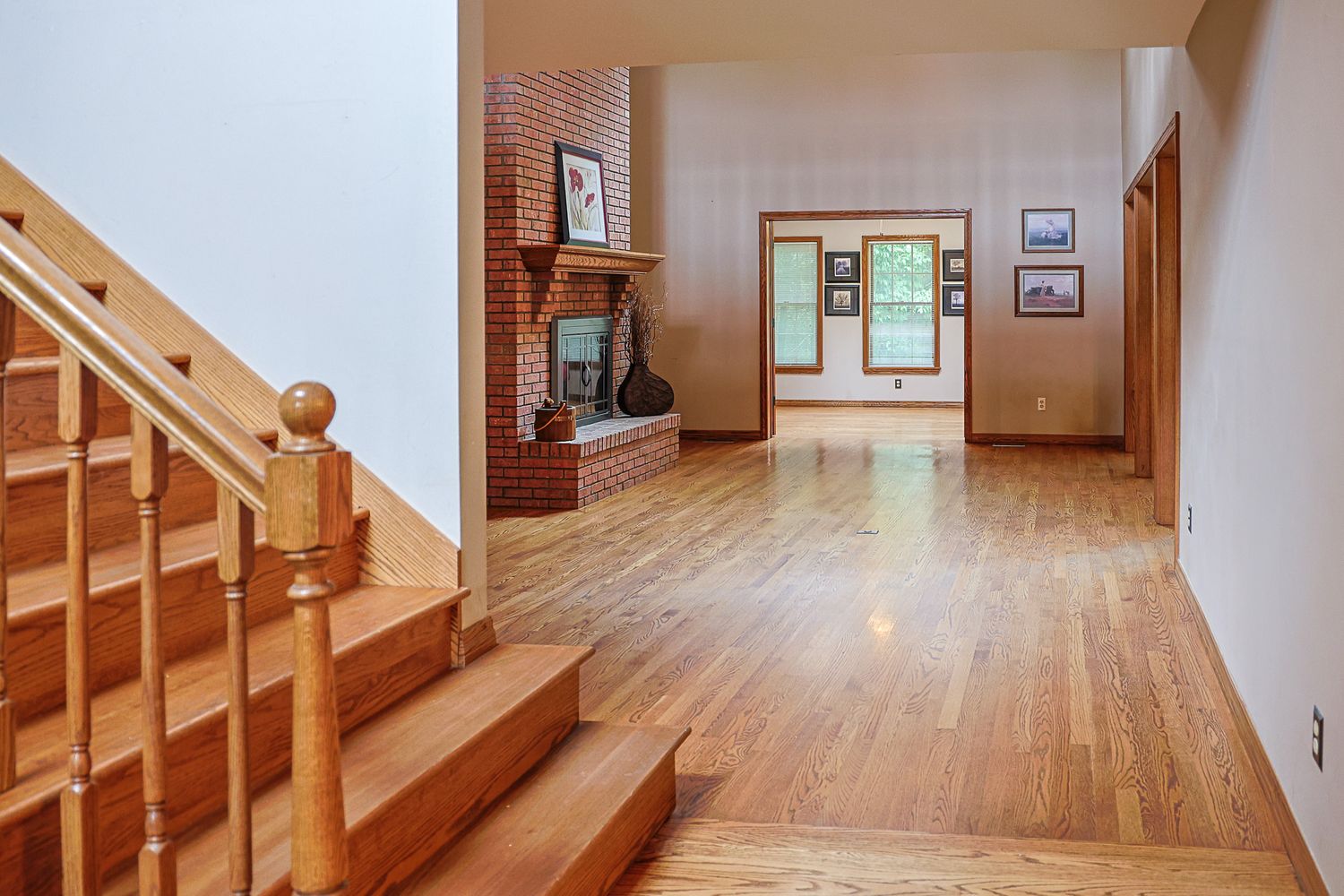 Bright home interior featuring hardwood floors, wooden staircase, brick fireplace, and open living area with natural light.