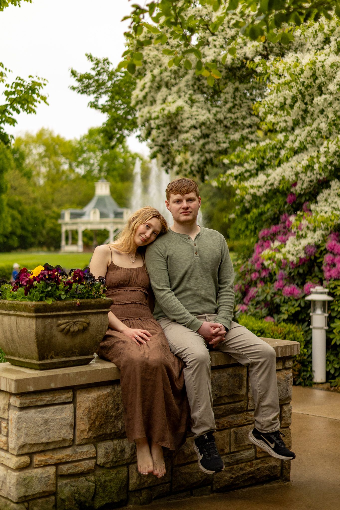 A couple sits together on a stone wall surrounded by blooming spring flowers and trees.