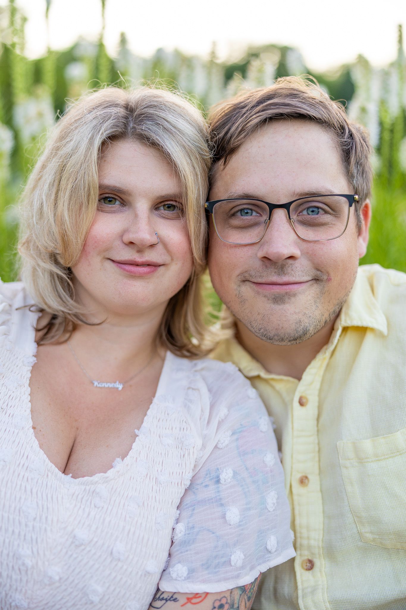Smiling couple posing together outdoors, woman with blonde hair and man wearing glasses.