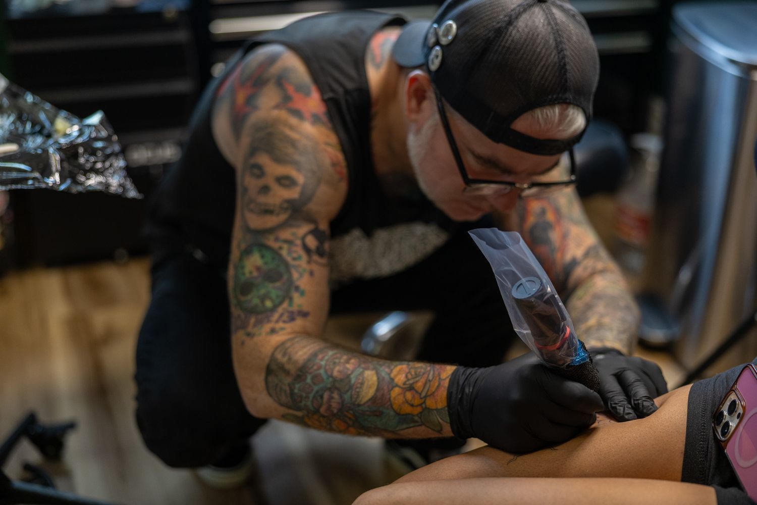 Heavily tattooed artist in black gloves carefully tattooing a client in a professional tattoo studio.