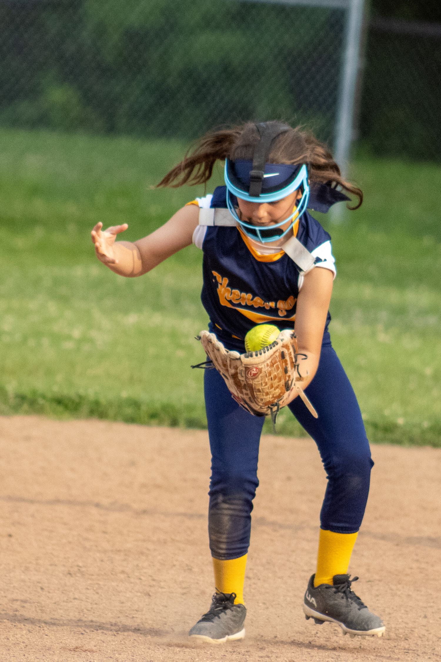 Youth softball player in navy uniform fields a ground ball during a game.