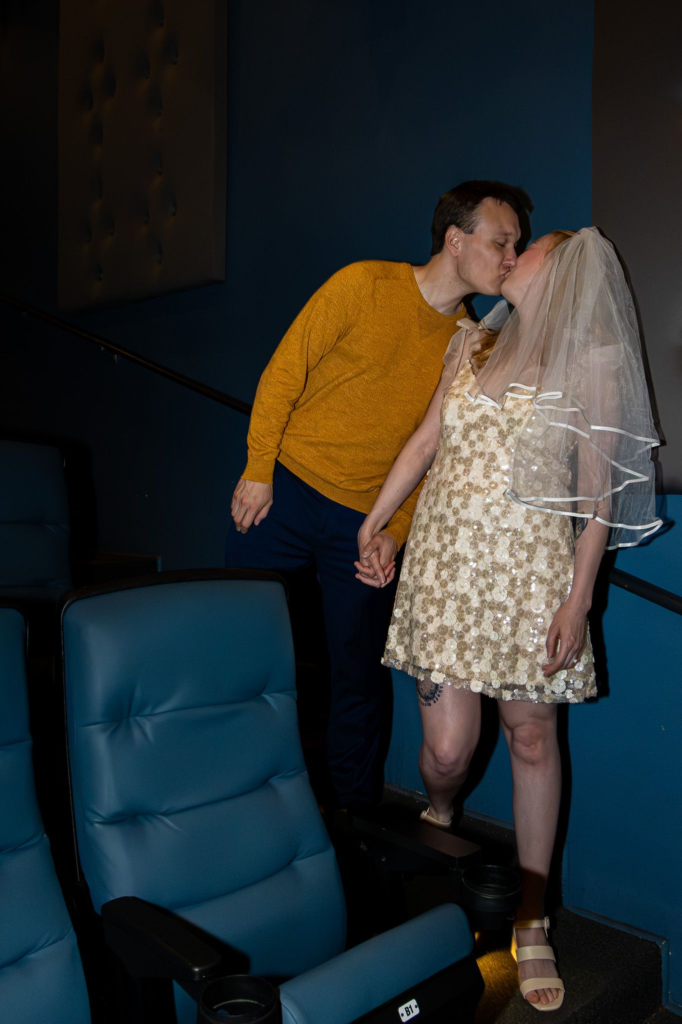 Couple kissing in movie theater aisle, bride wearing veil and floral dress.
