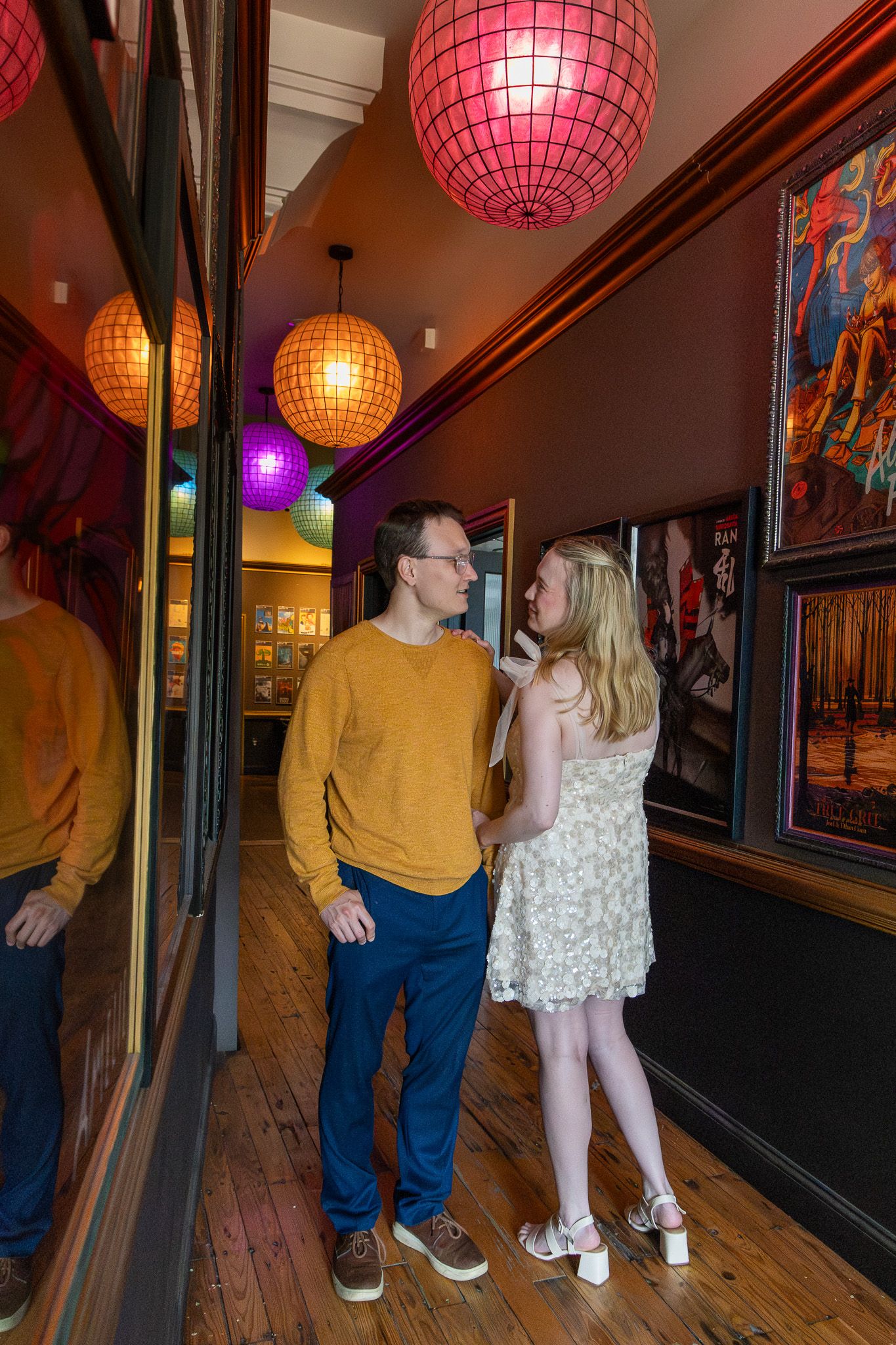 Couple sharing romantic moment in vibrant hallway with glowing pink pendant lights above.