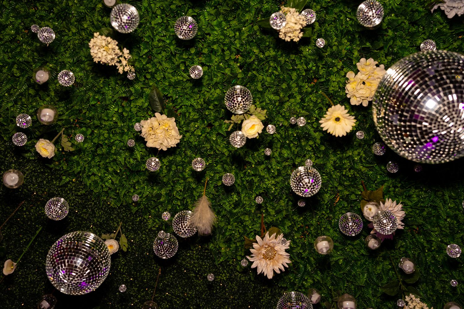 Elegant wedding decor featuring disco balls and white flowers arranged on a lush green wall.