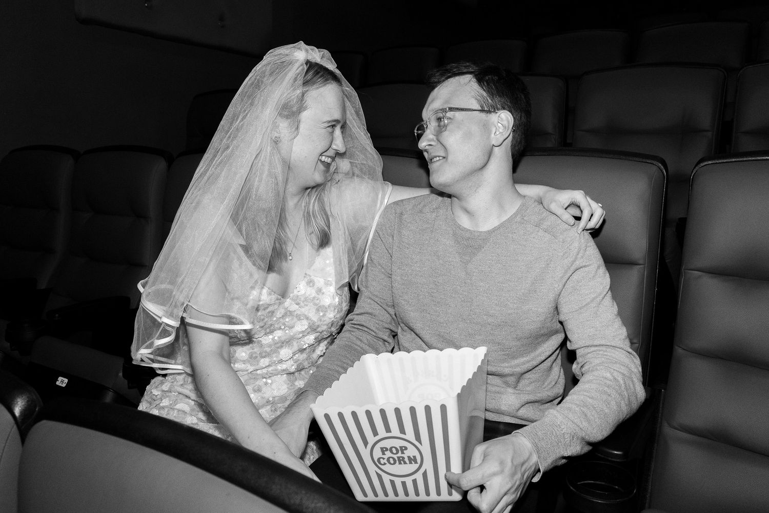Black and white photo of bride in veil and groom smiling at cinema.