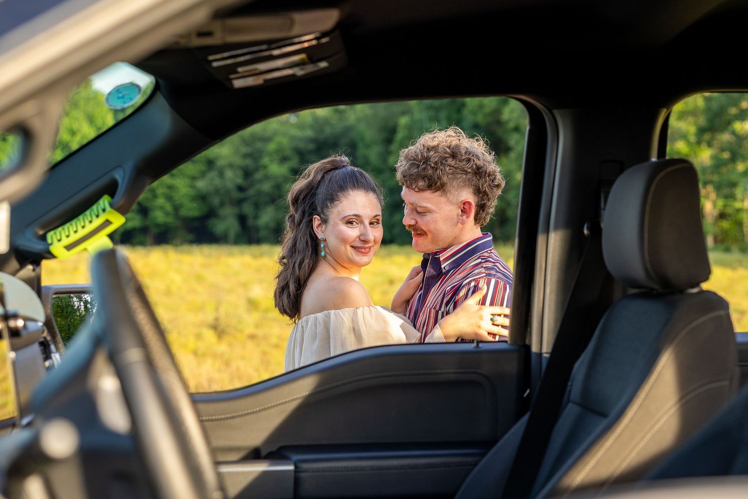 A couple shares an intimate moment viewed through a truck window with a field backdrop.