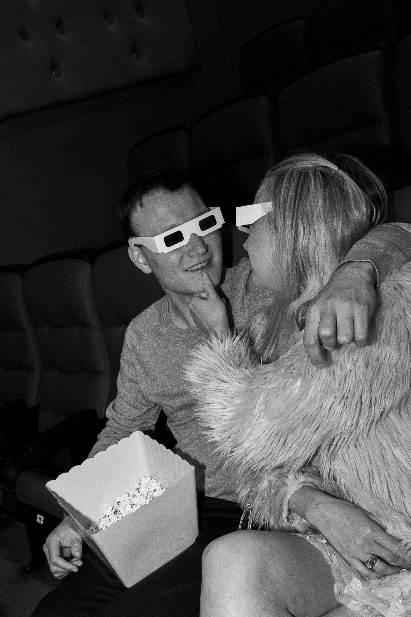 Black and white photo of couple with 3D glasses sharing popcorn at movies.