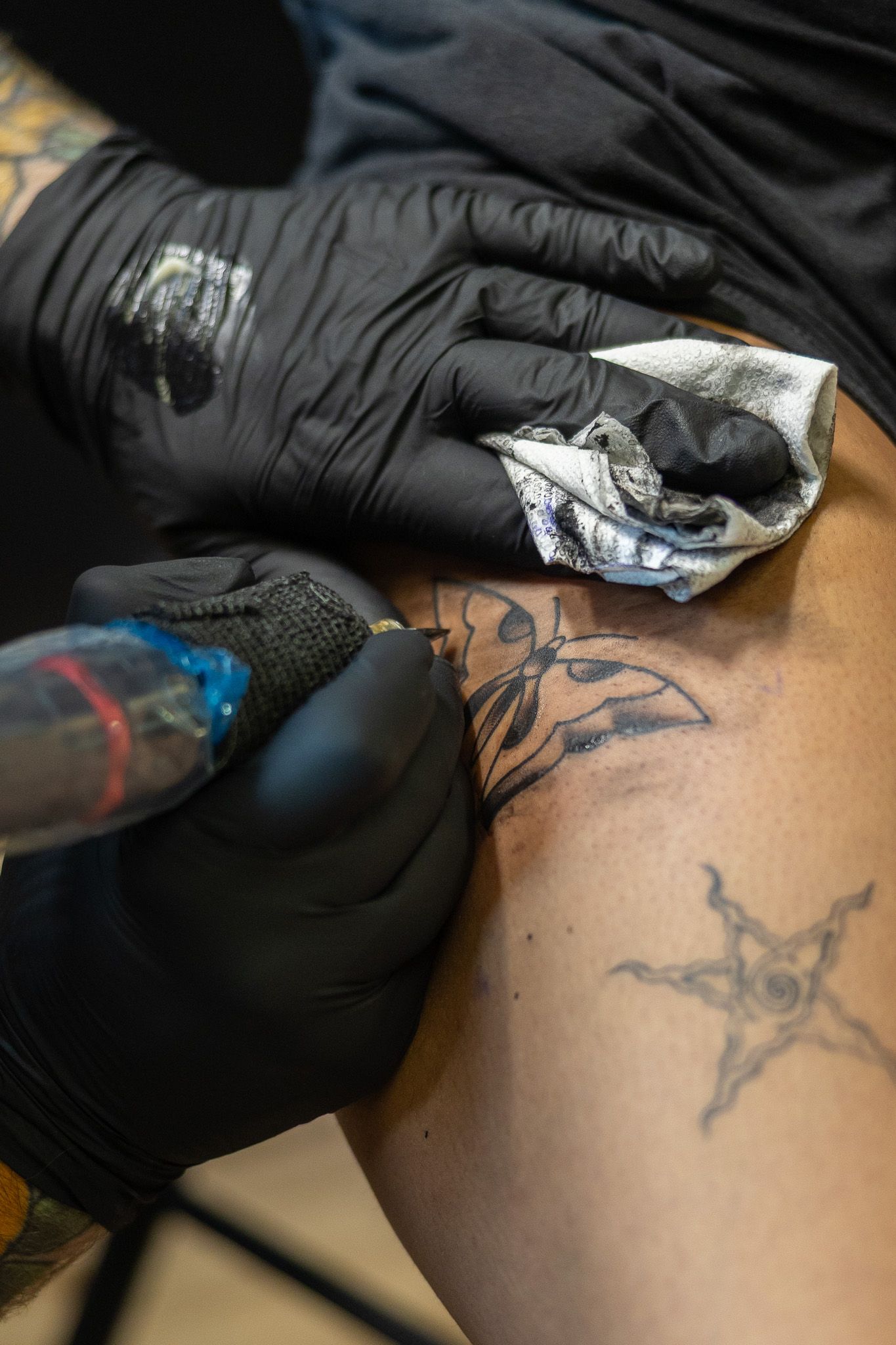Close-up of tattoo artist in black gloves applying ink to a tribal tattoo design on a client's leg.