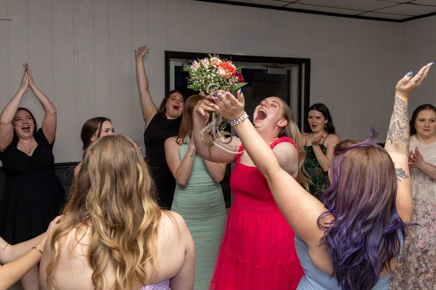 Excited women reach for a tossed bridal bouquet during a lively wedding reception bouquet toss.