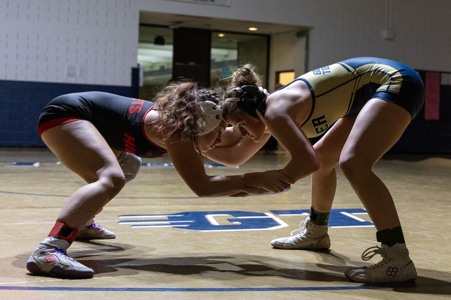Two female wrestlers face off in starting position on a blue mat indoors.