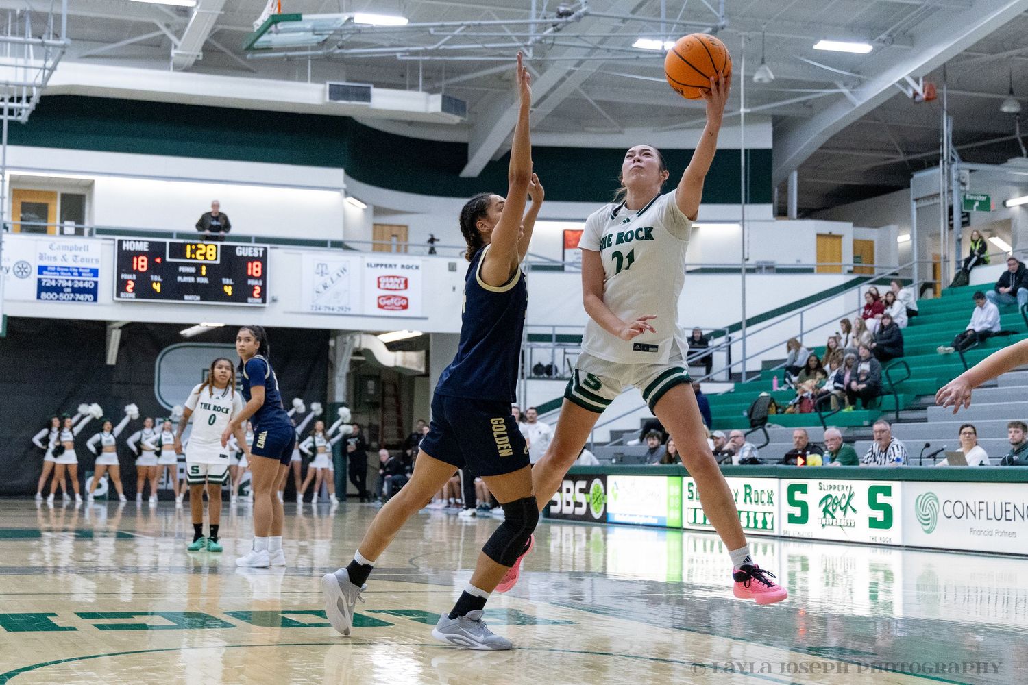Female basketball player number 11 jumps for layup against defender in packed gymnasium.
