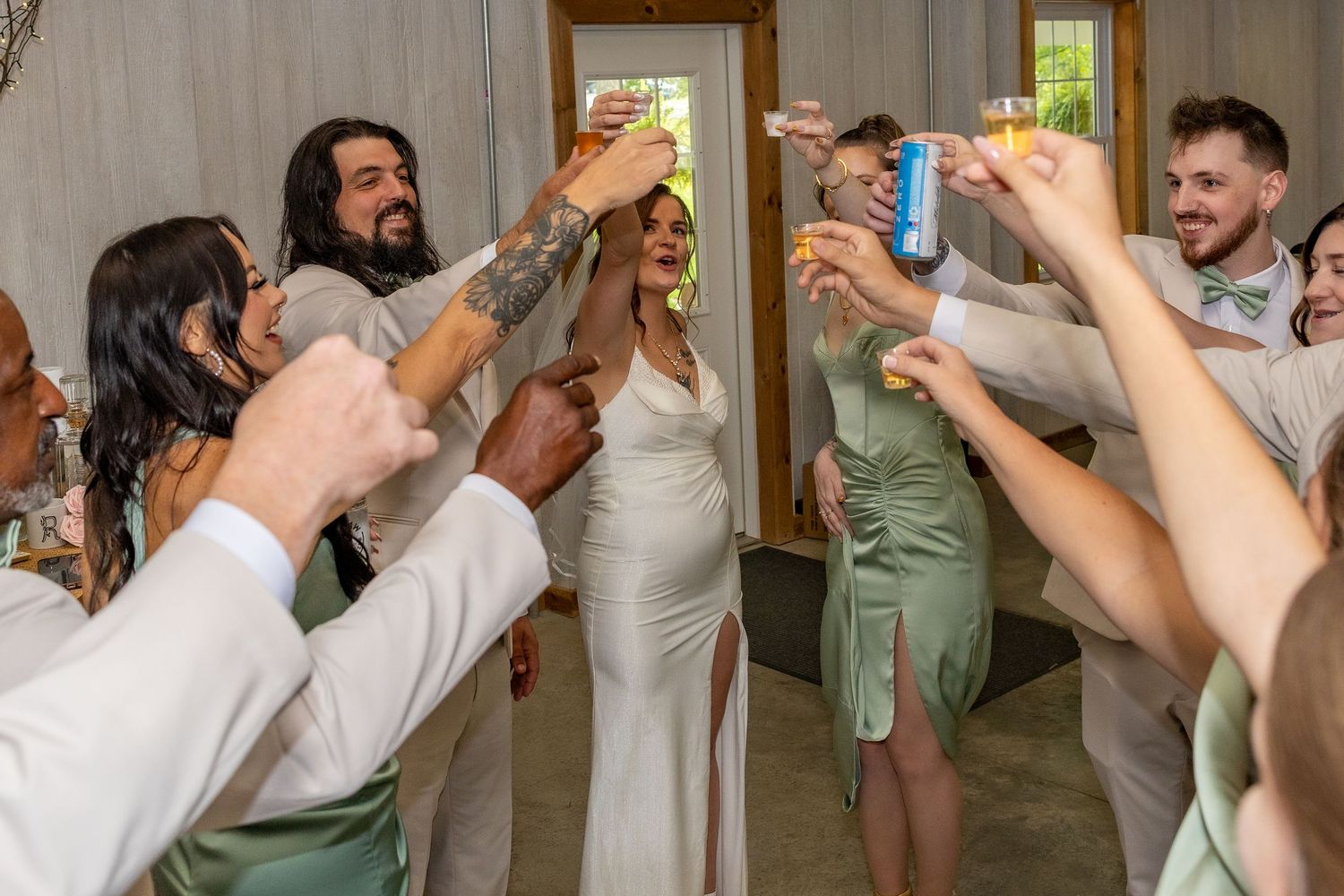 Bride and groom toast with wedding party guests raising drinks in celebration at a rustic indoor wedding reception.