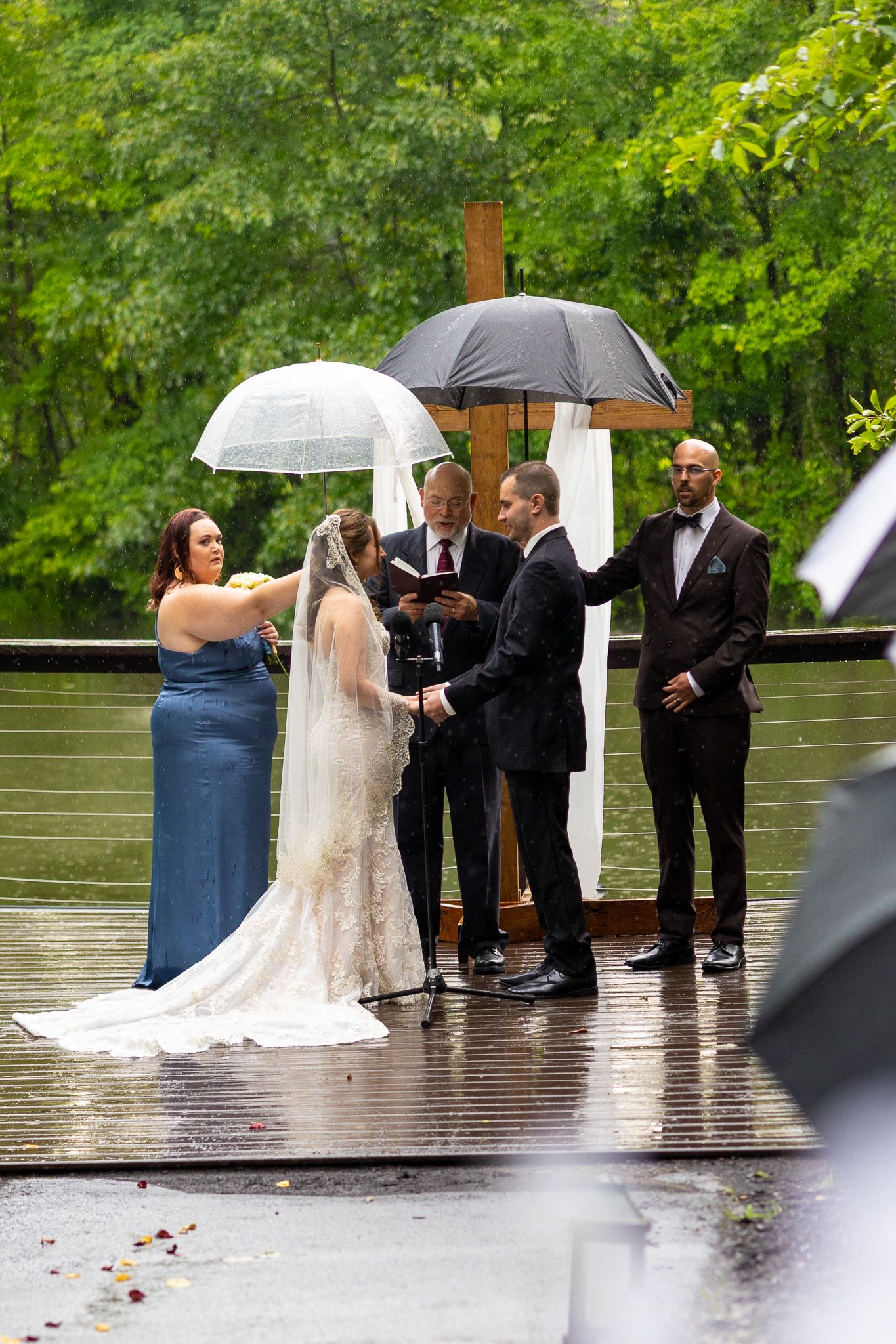 Bride and groom exchange vows during rainy outdoor wedding ceremony on dock with umbrellas and officiant.